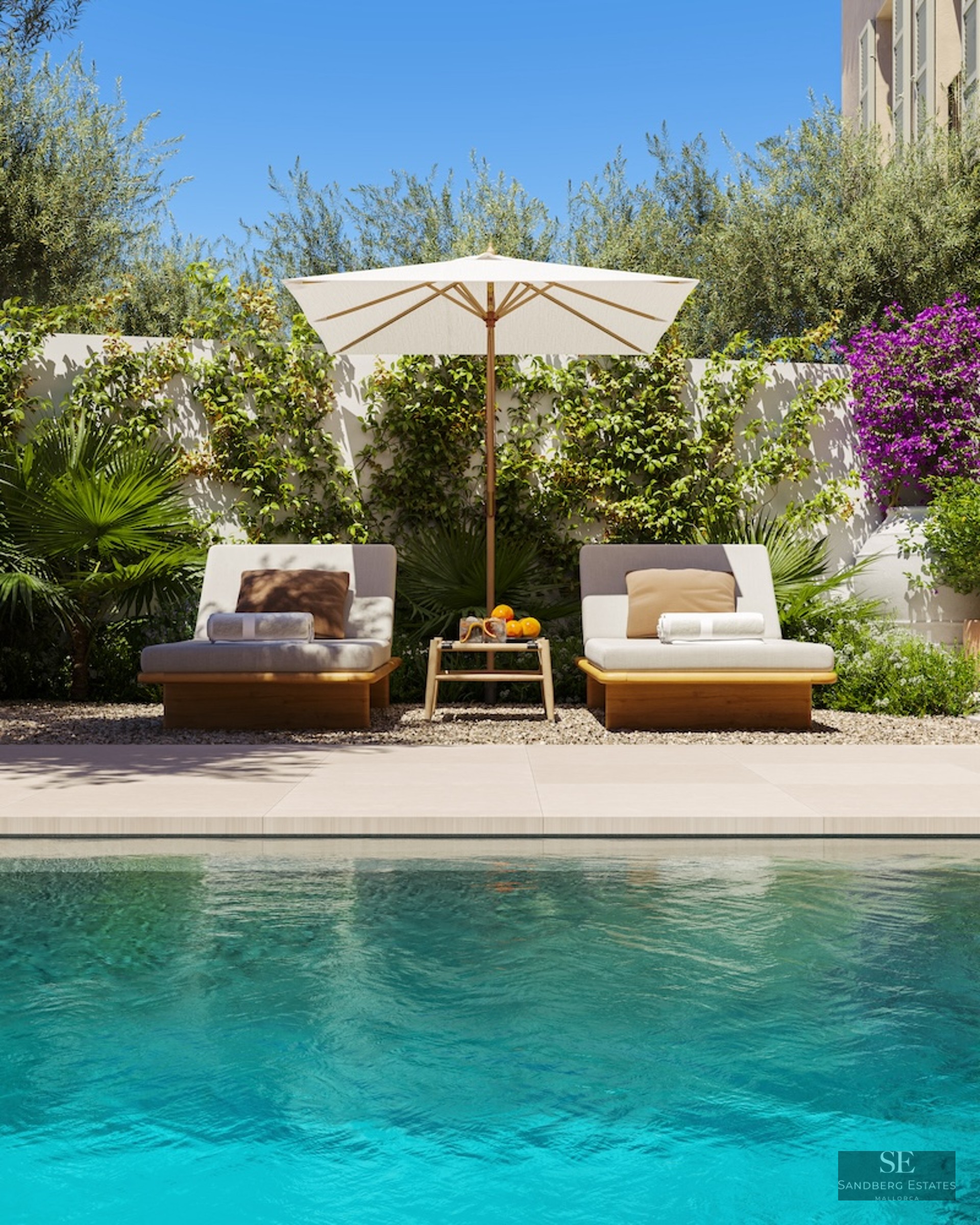Two sun loungers with a white umbrella next to a turquoise pool surrounded by bougainvillea and olive trees.