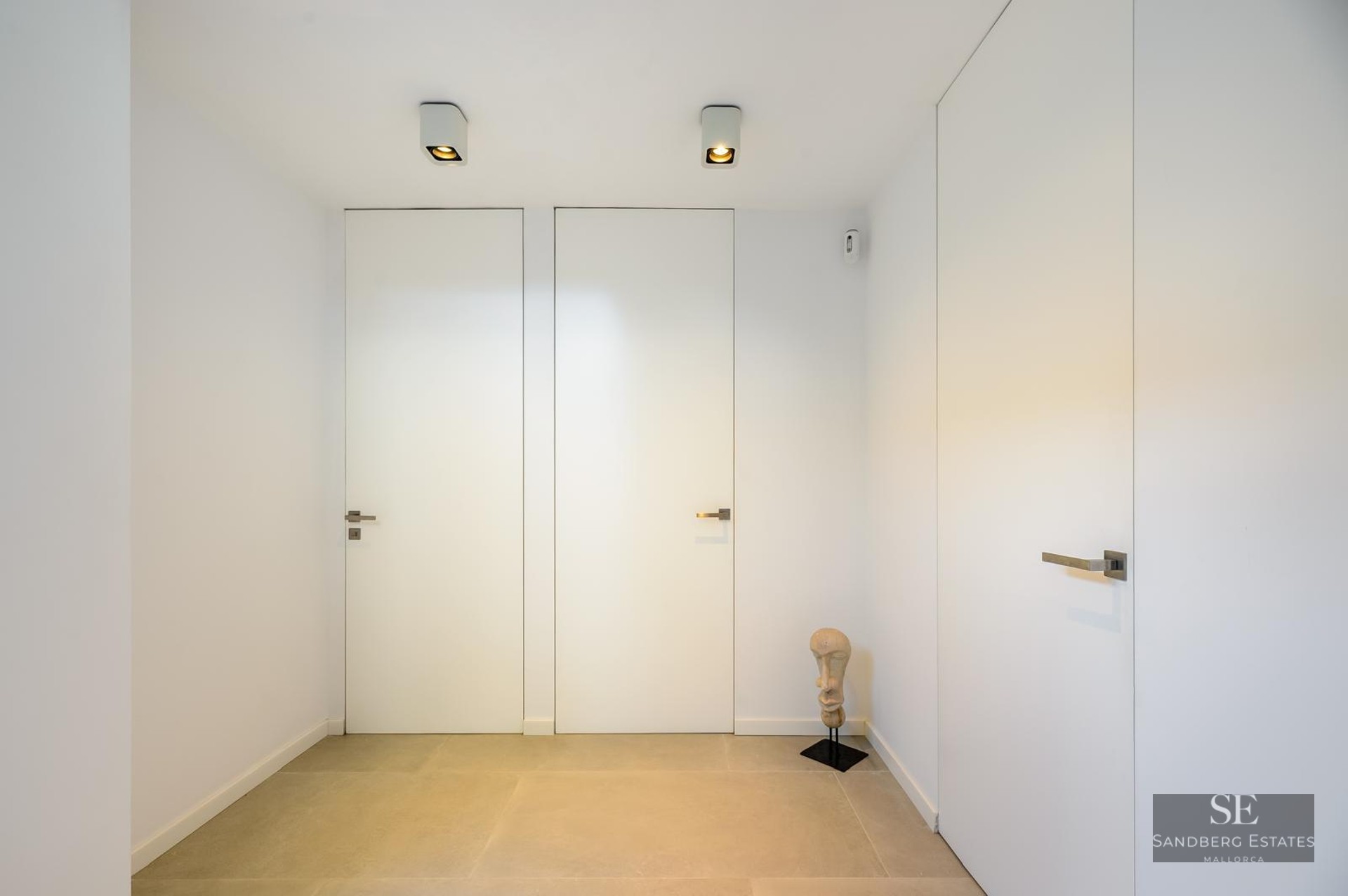 Minimalist hallway with flush white doors, light stone flooring, and a small decorative head sculpture.