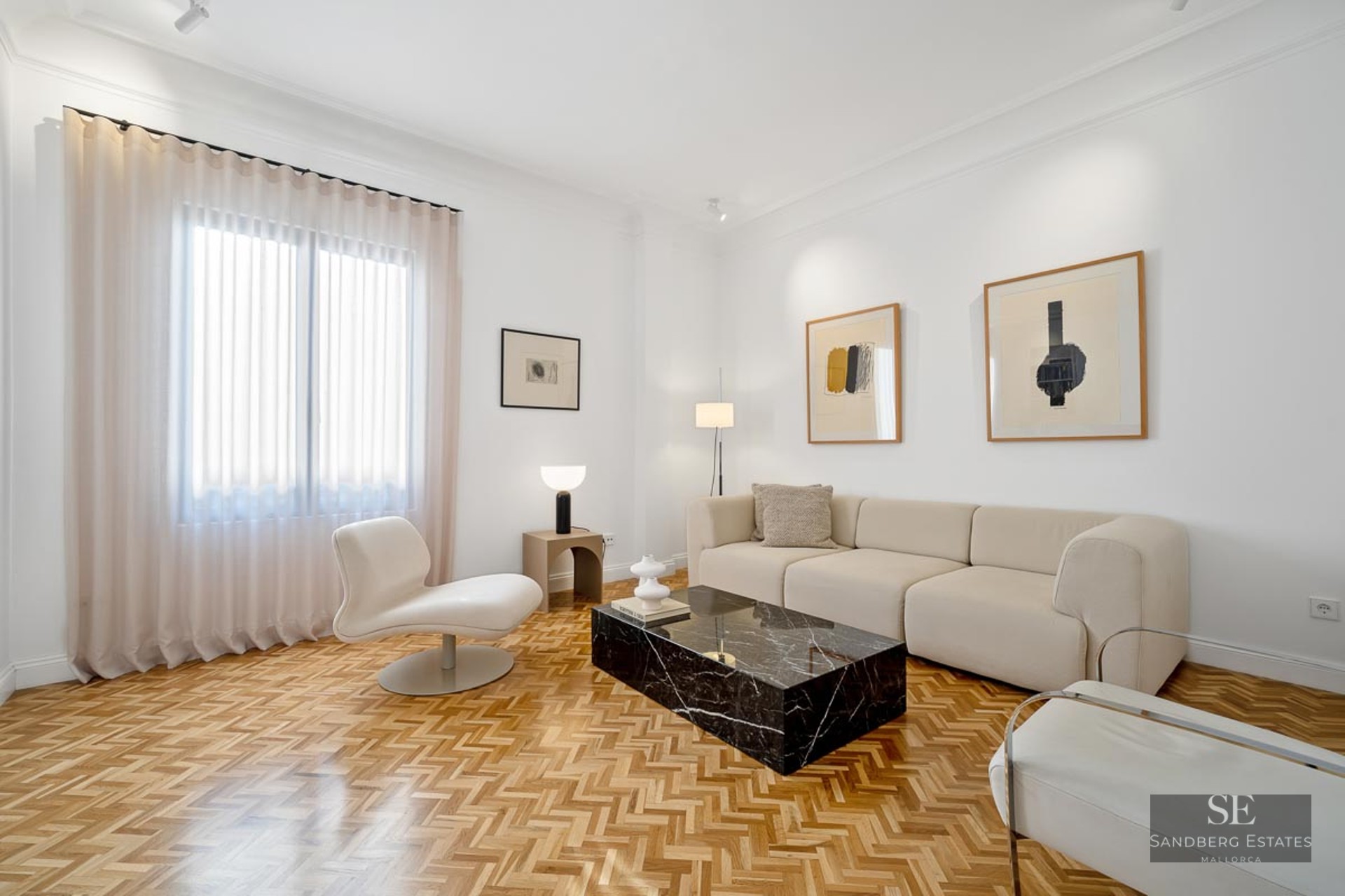 Bright living room with white walls, herringbone wood floors, a beige sofa, and a black marble coffee table.