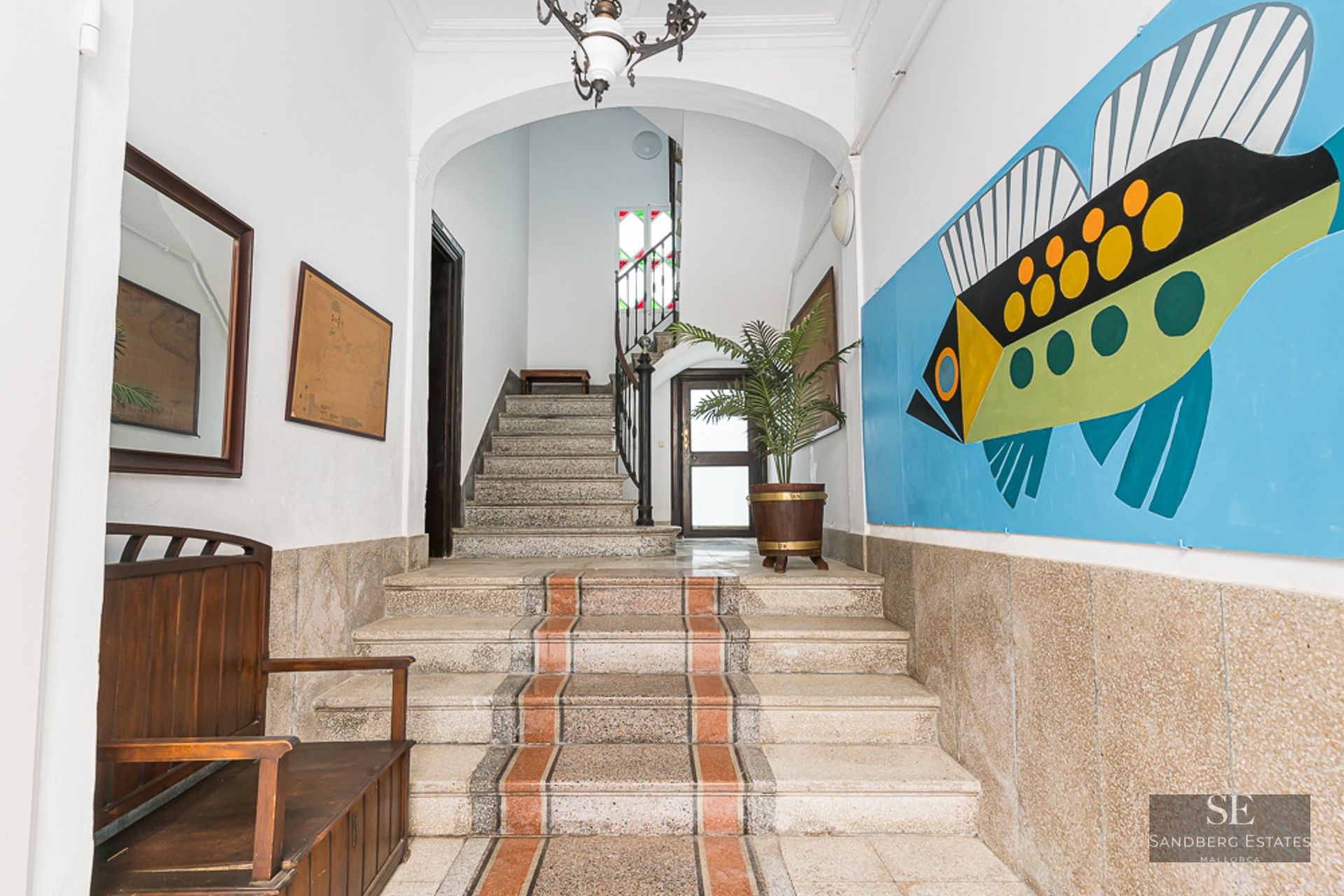 Entrance with stone stairs, wooden bench, and a large colorful fish mural on the wall.