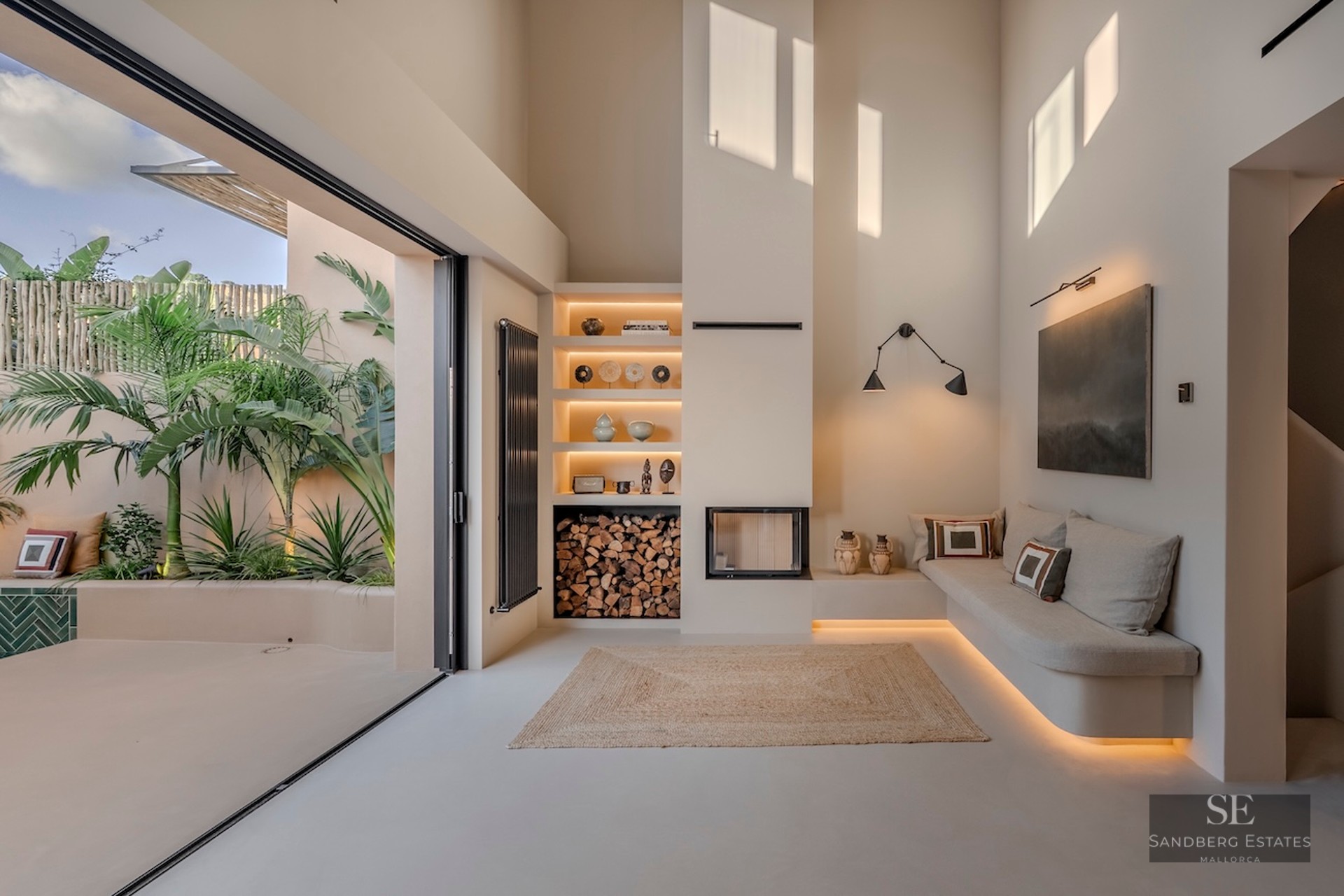 Salon épuré avec cheminée intégrée, banquette sur mesure et grandes baies vitrées donnant sur un jardin tropical.