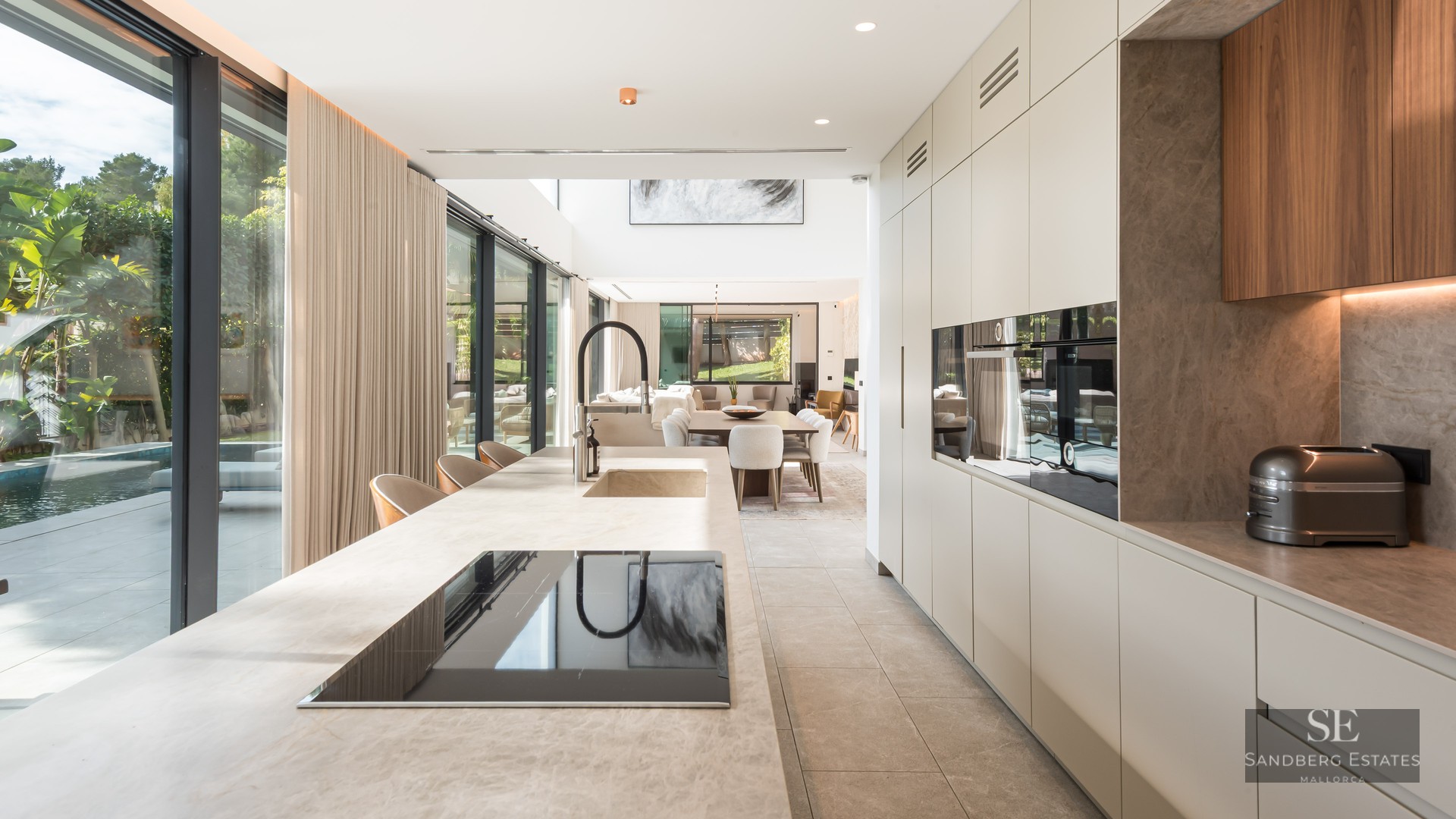 Cuisine moderne avec un grand îlot en pierre, des appareils intégrés et des baies vitrées donnant sur une piscine.