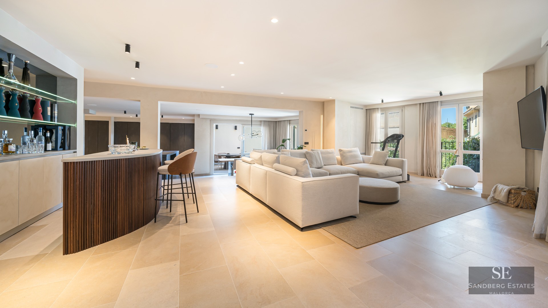 Spacious modern living room with a large white sofa, wooden bar counter, and natural stone flooring.