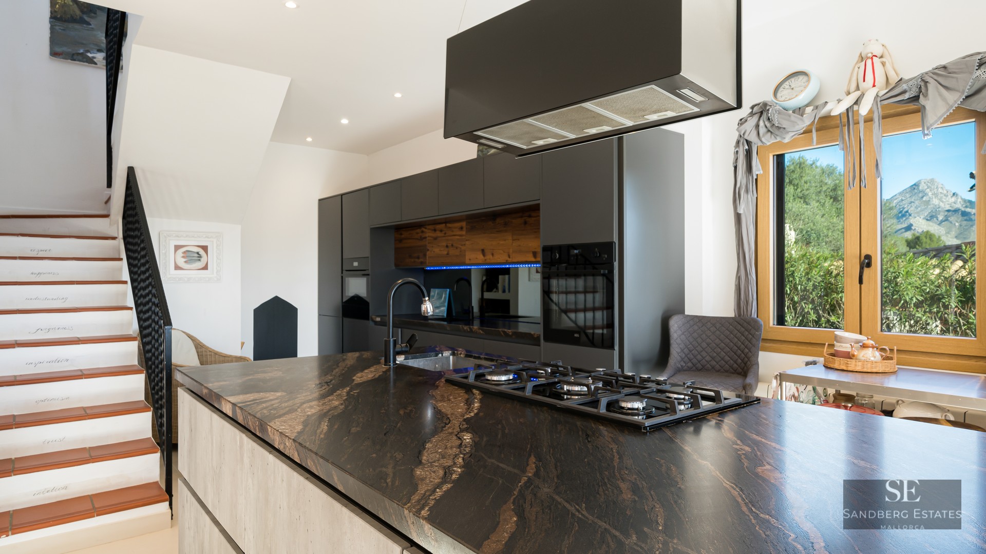Modern kitchen featuring a large black marble island with a gas stove and a view of mountains through a window.