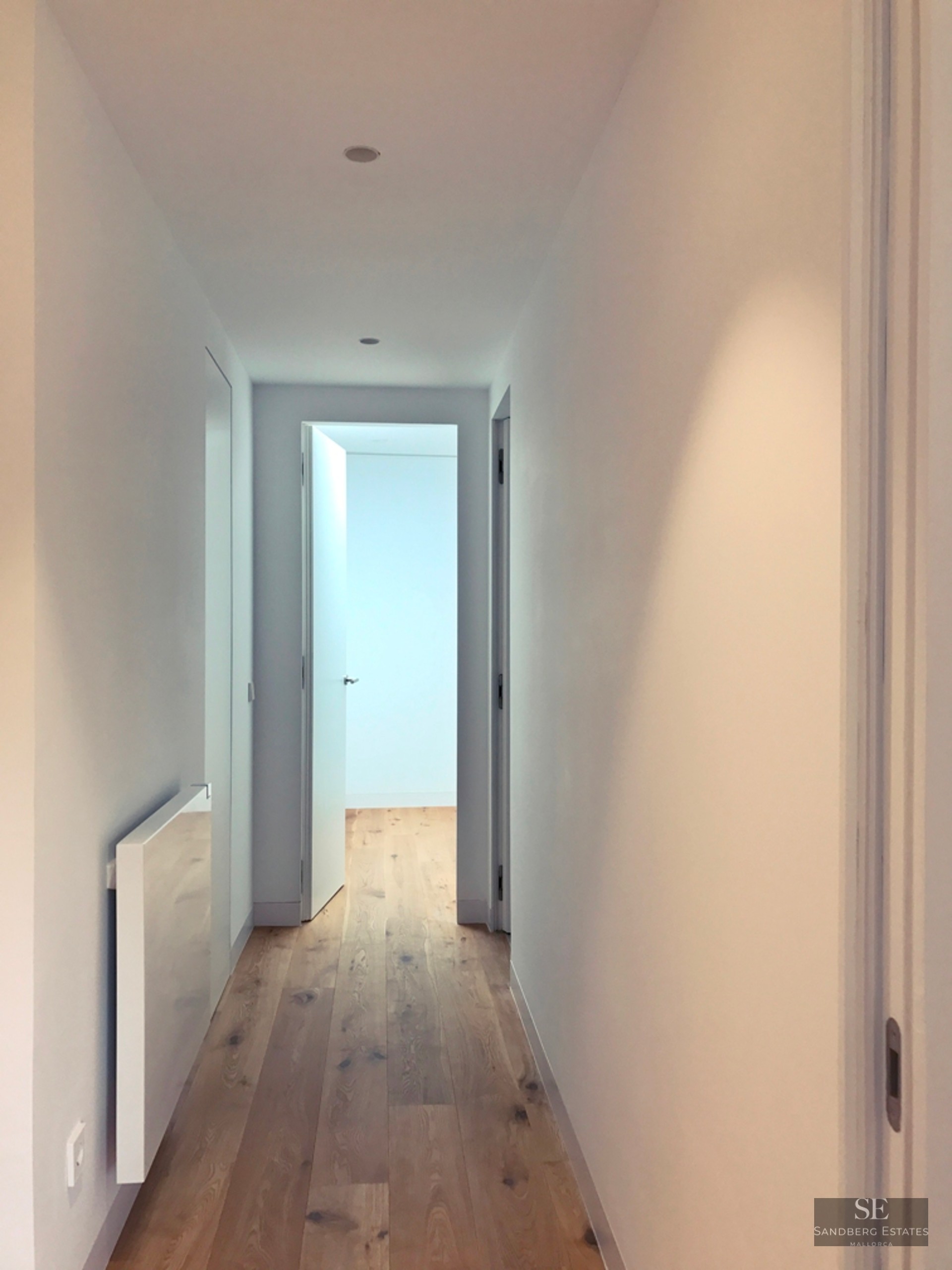 Narrow white hallway with light oak wood floors and minimalist white doors.