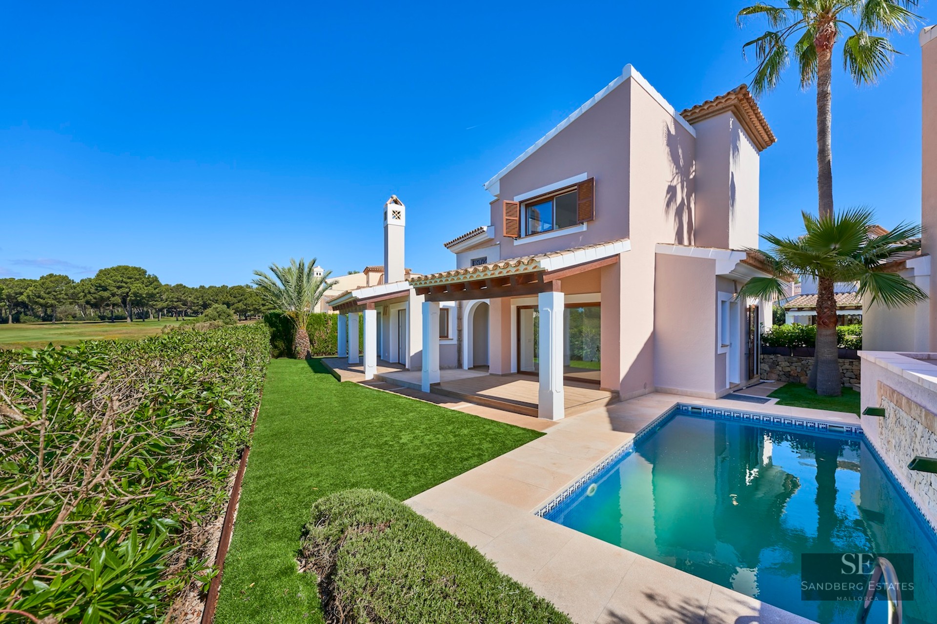 Modern Mediterranean villa featuring a private swimming pool, lush green lawn, and palm trees under a clear blue sky.