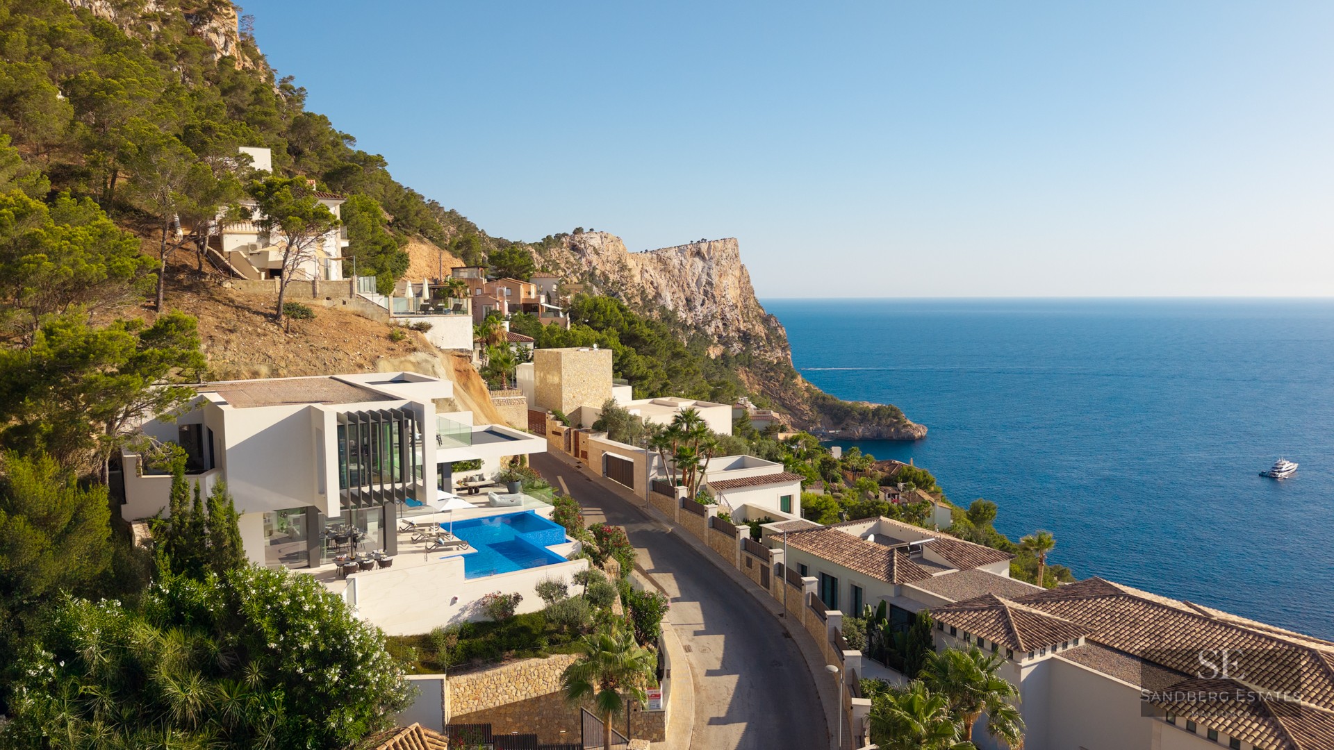 Aerial view of a white modern villa with an infinity pool on a cliffside overlooking the blue Mediterranean sea.