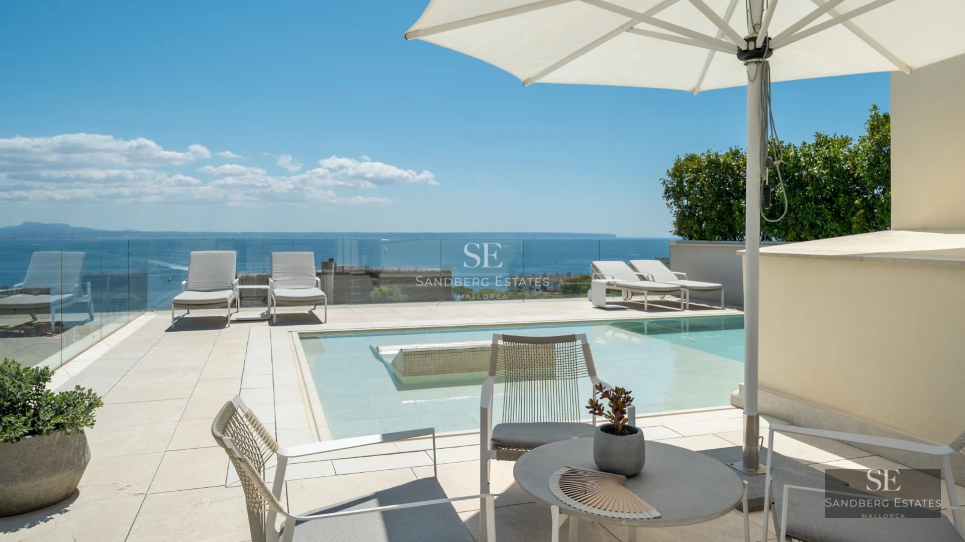 Spacious balcony with panoramic sea views. Glass railing, wooden floor, modern outdoor furniture. Soft lighting and relaxing atmosphere.