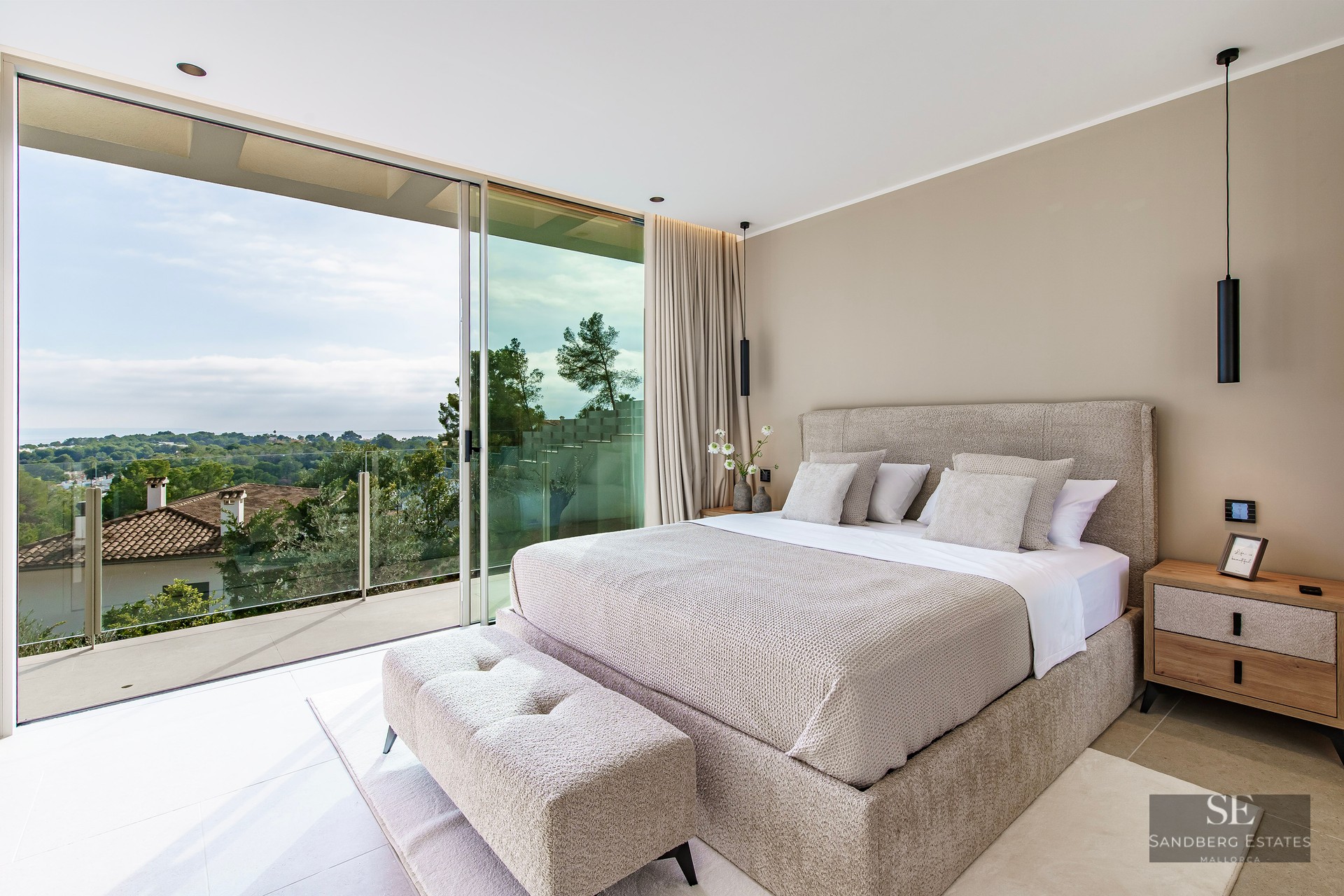 Luxury bedroom with a beige bed and floor-to-ceiling glass doors opening to a balcony with a scenic green view.