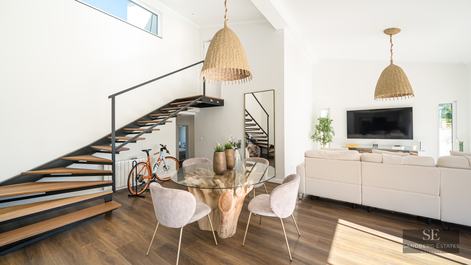 Salon lumineux à aire ouverte avec table en bois flotté, chaises en velours et escalier flottant en bois.