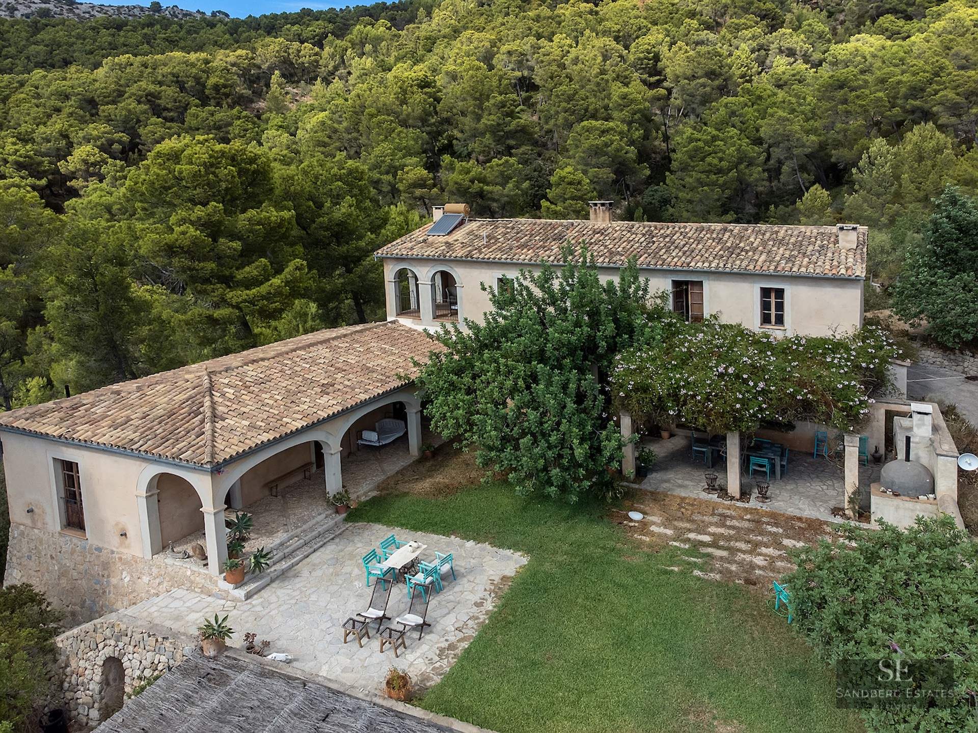 Aerial view of a traditional stone villa with terracotta roofs and arched patios surrounded by dense green forest.