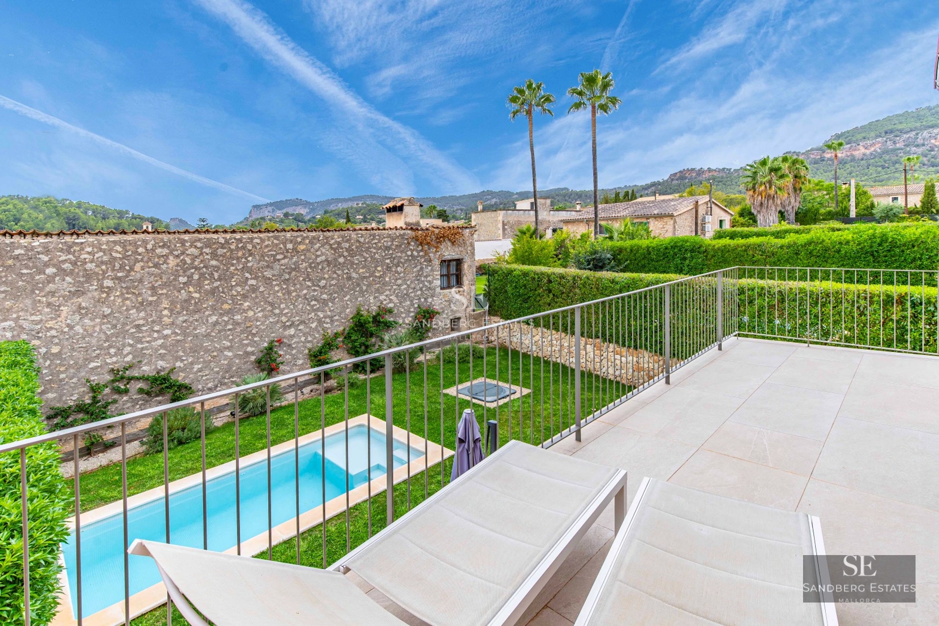 View of infinity pool with sundeck, sun loungers and lush garden. Modern design with ambient lighting.