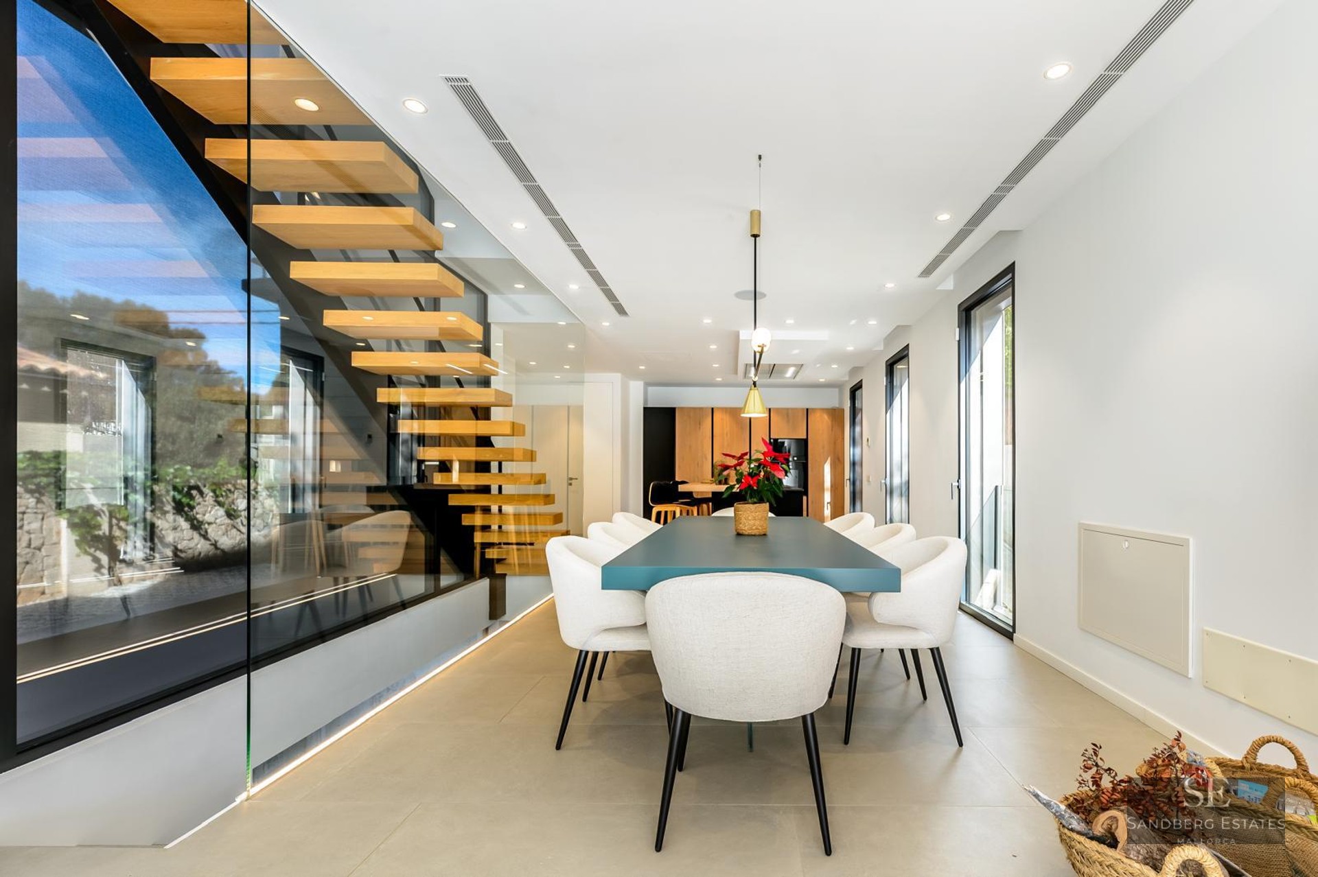 Modern dining room featuring a teal table, white chairs, and a glass-enclosed floating wooden staircase.