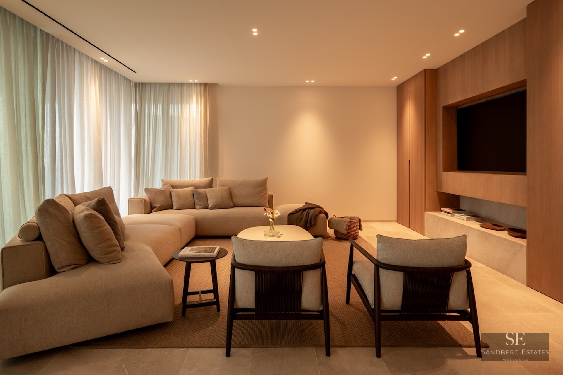 Elegant living room with large beige modular sofa, wooden wall paneling with integrated TV, and warm lighting.