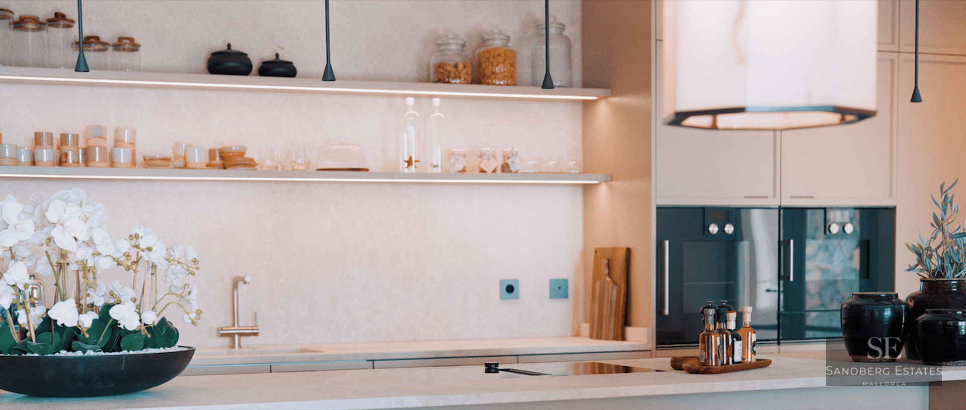 Close-up of a luxury kitchen featuring cream stone countertops, LED-lit open shelving, and integrated appliances.
