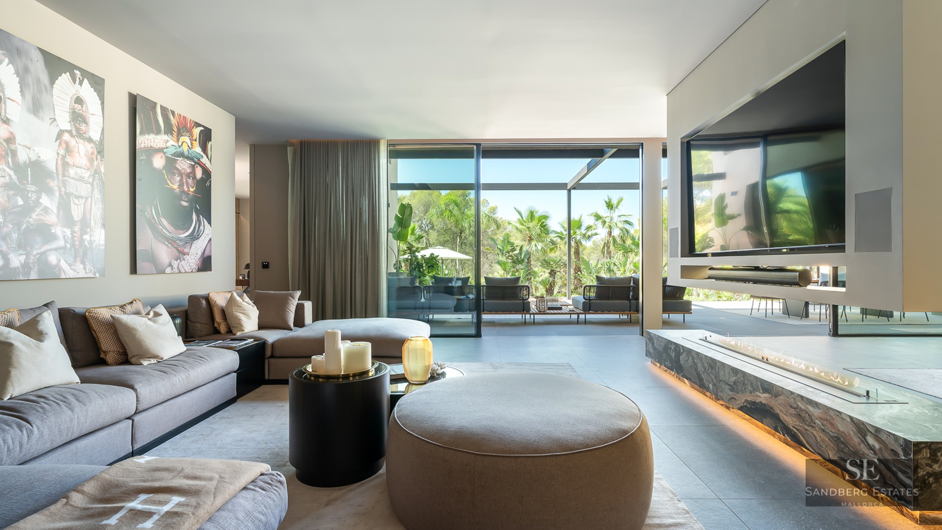 Modern living room with grey sectional sofa, linear fireplace, and floor-to-ceiling glass doors opening to a garden.