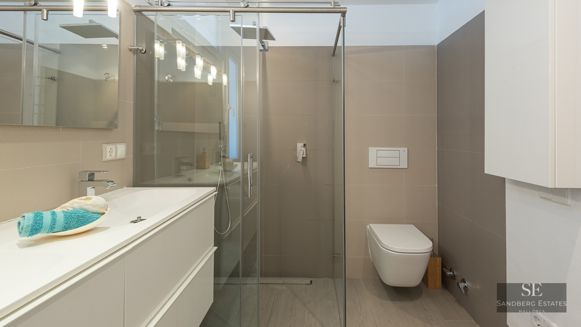 Modern bathroom featuring a white vanity, glass shower enclosure, and a wall-mounted toilet with neutral tiling.
