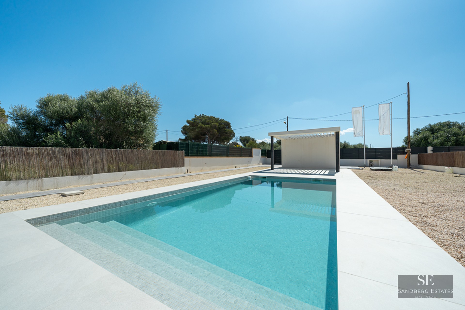 Rectangular turquoise pool with white tile border and a modern white pergola under a clear blue sky.