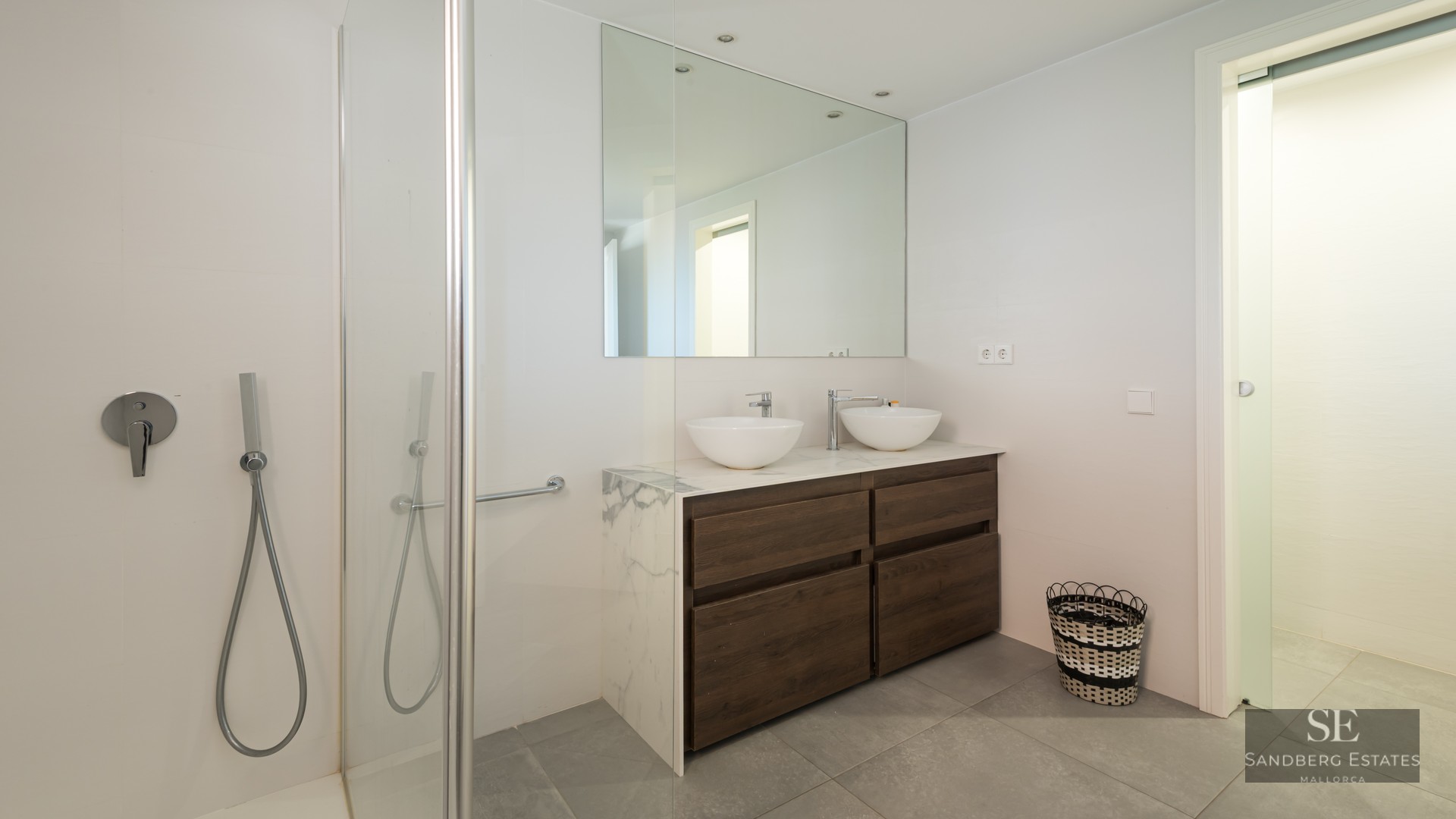 Bright modern bathroom featuring a wood double vanity with marble top, twin vessel sinks, and a glass shower.