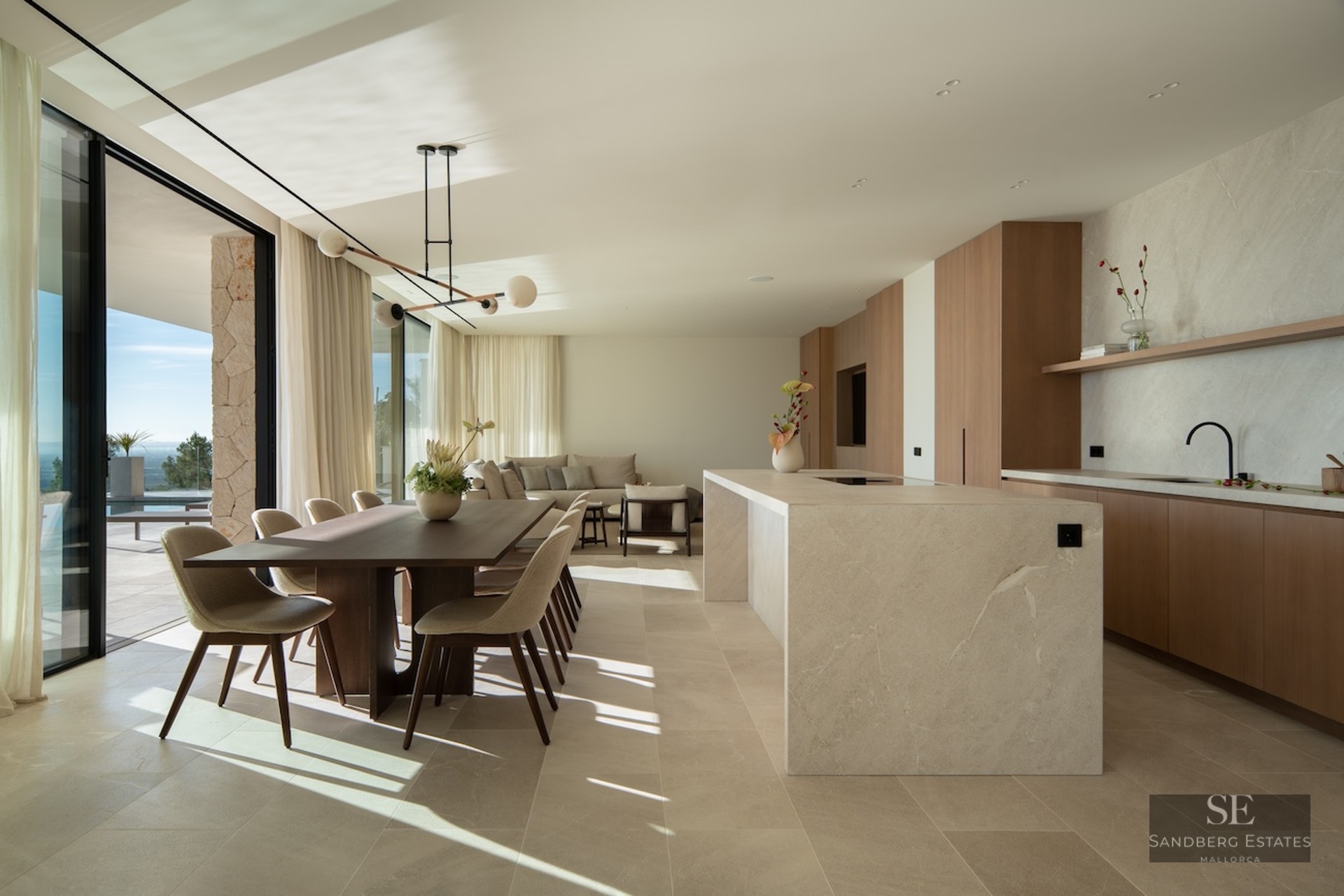 Spacious open-concept room featuring a stone kitchen island, wooden dining table, and floor-to-ceiling terrace doors.