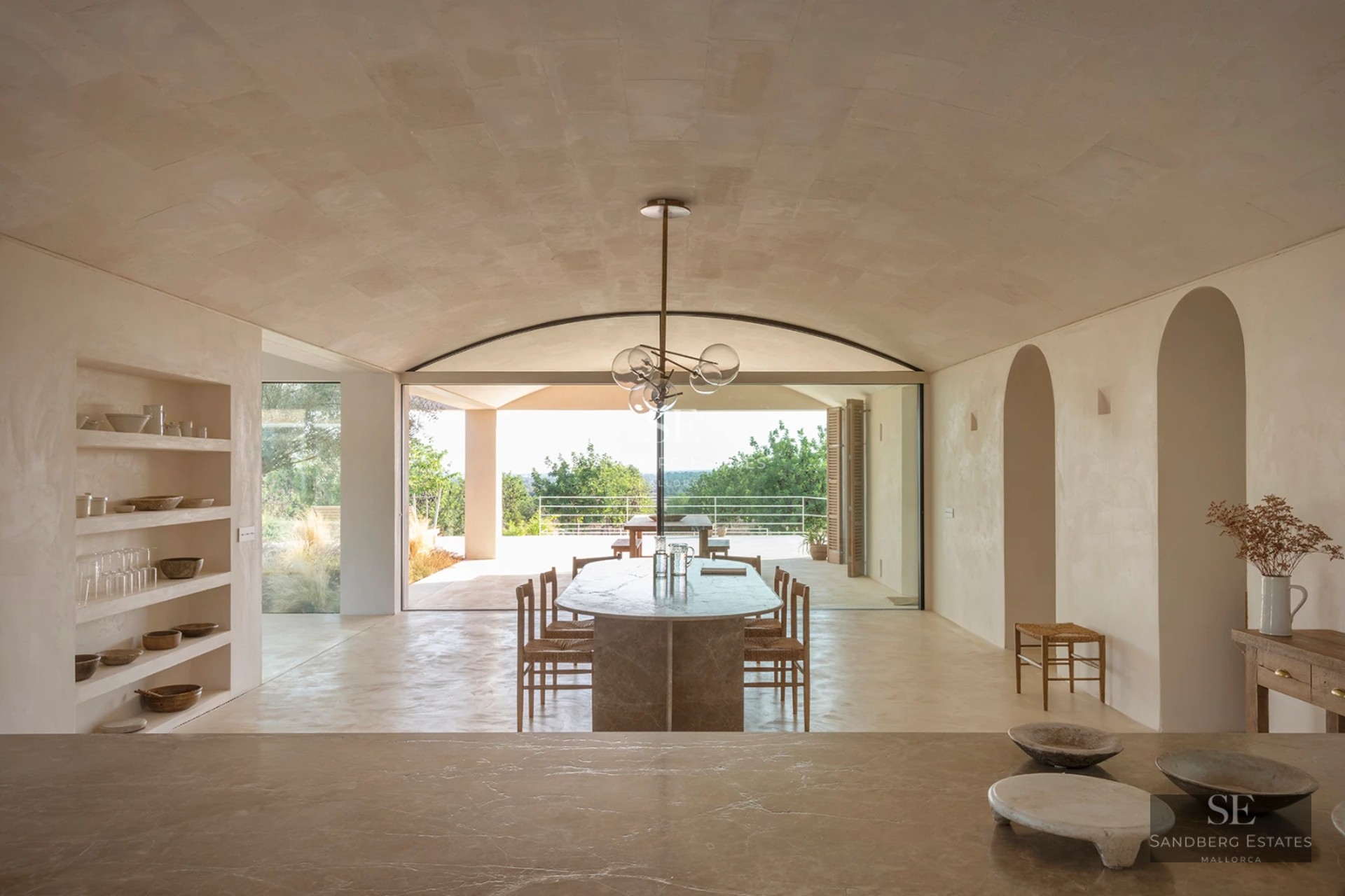 Large swimming pool with sun loungers, umbrellas, and lush greenery. Modern house in the background with large windows and a balcony.