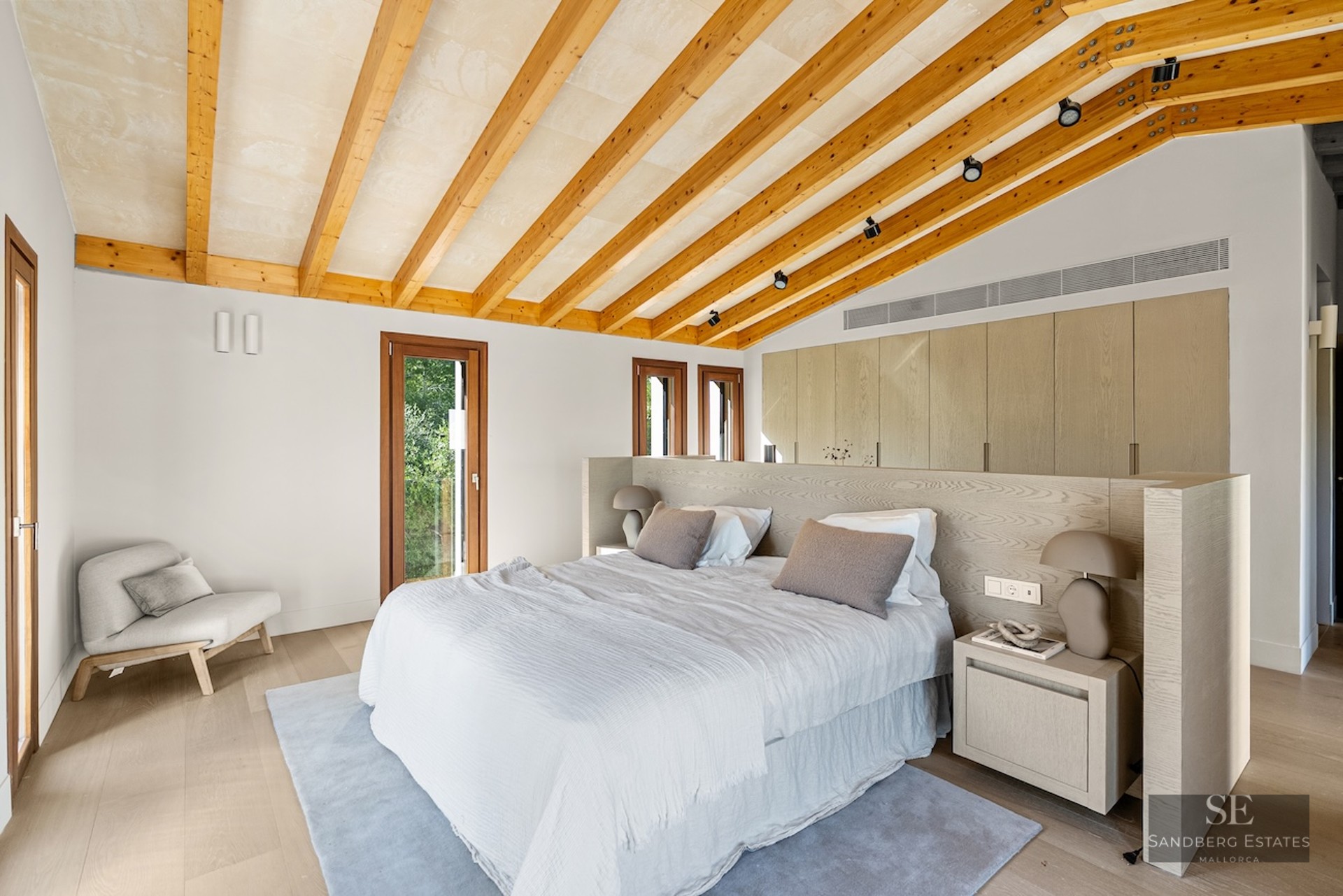 Modern master bedroom with vaulted ceiling, wooden beams, large bed, and built-in wardrobes.