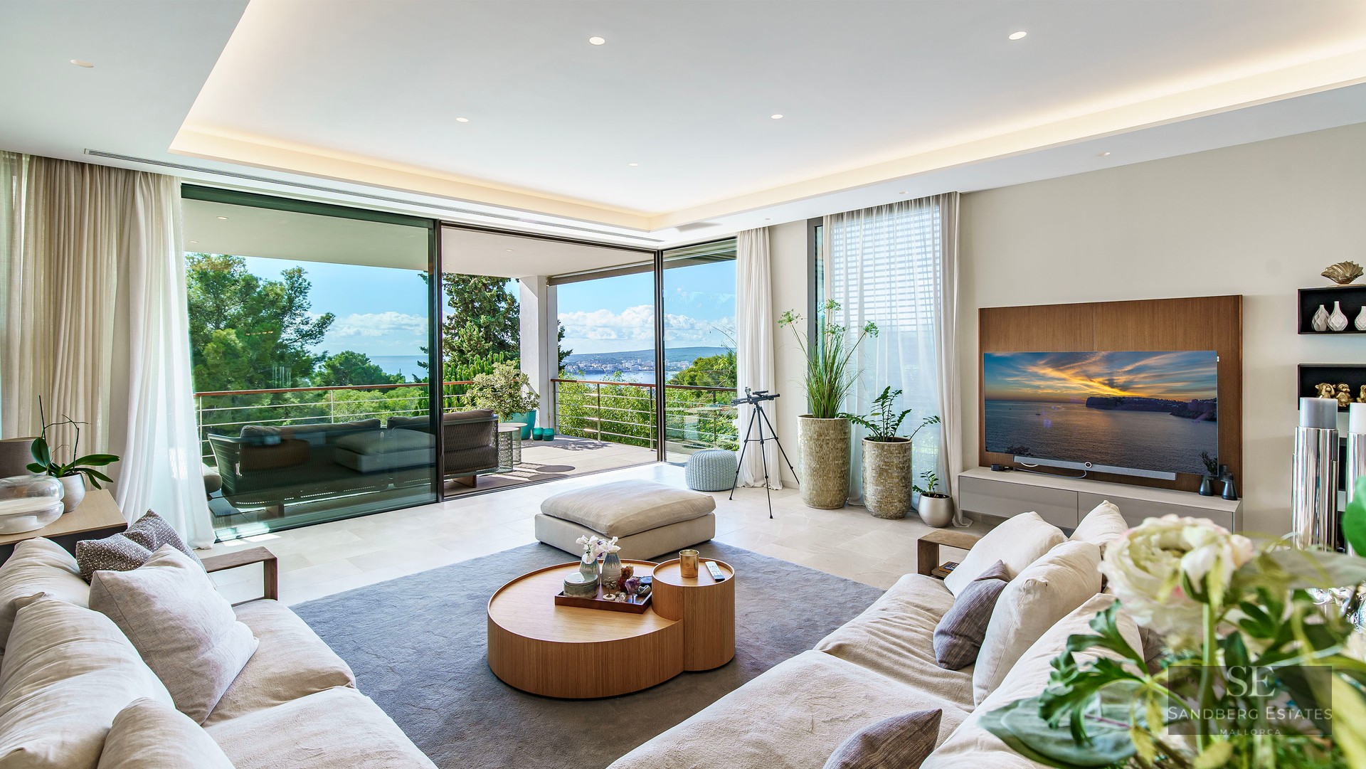 Salon moderne avec baies vitrées du sol au plafond s'ouvrant sur une terrasse avec vue sur mer.