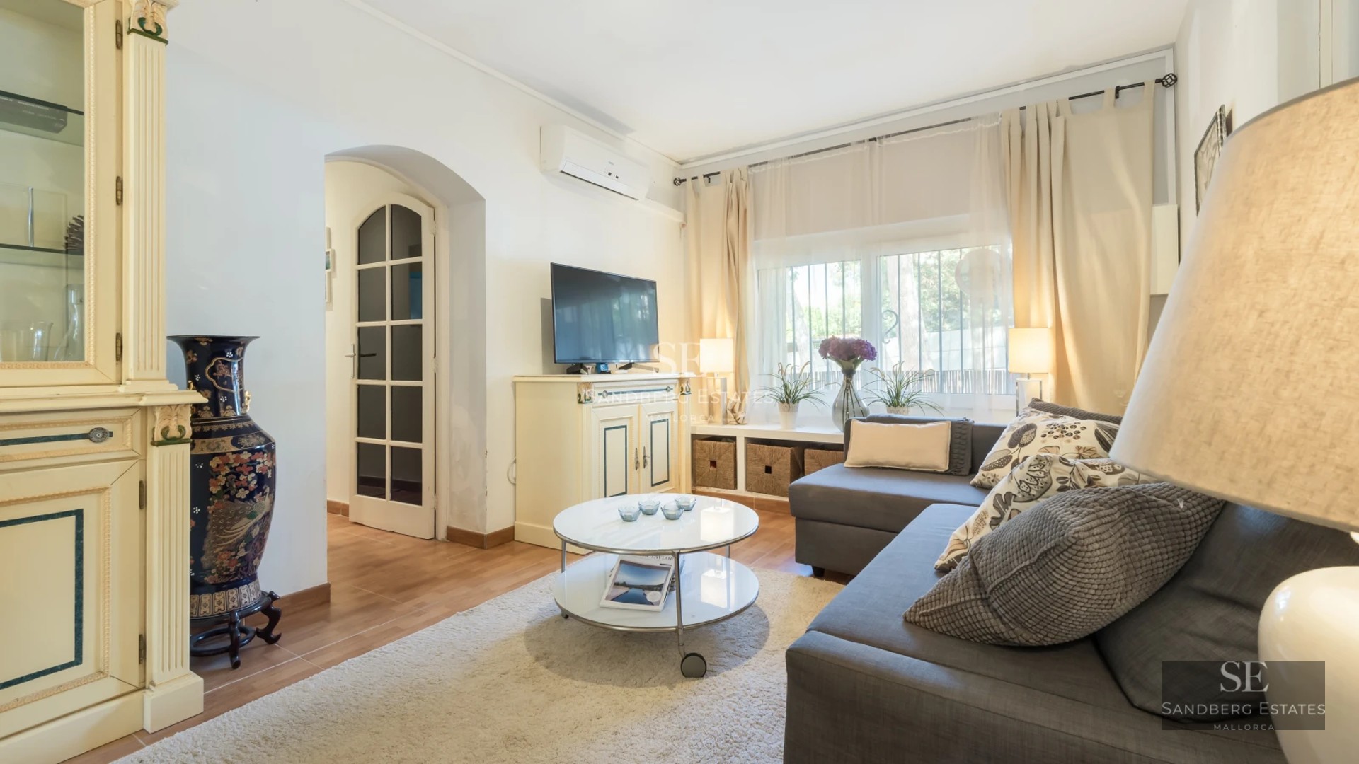 Spacious living room with floor-to-ceiling windows, light wood floors, and modern furniture. Abundant natural light. Garden view.