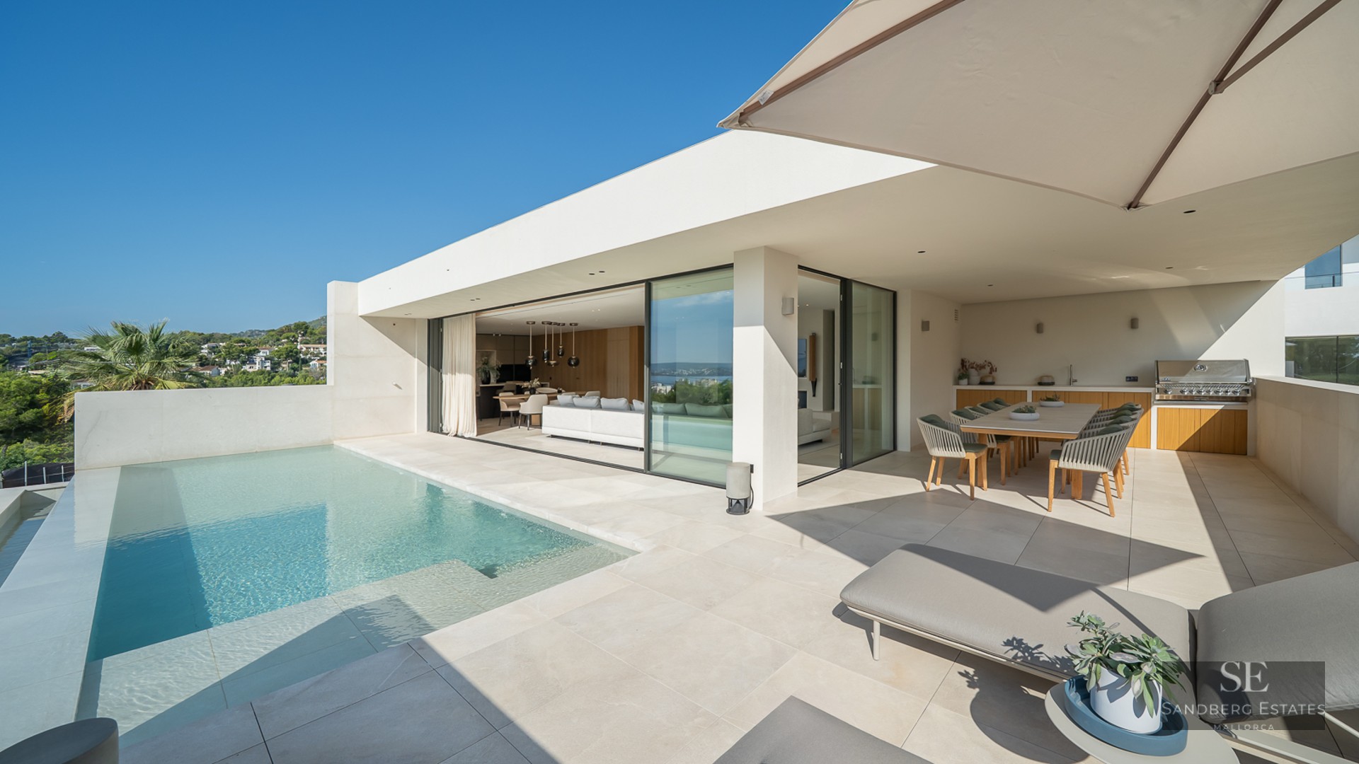 Modern villa terrace with infinity pool, sun loungers, outdoor dining area, and seamless indoor-outdoor living space.