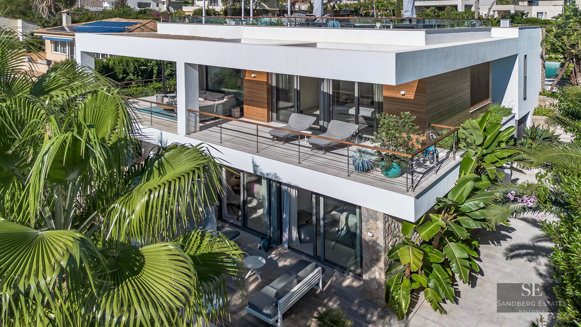 Vue aérienne d'une villa moderne blanche de deux étages avec balcons en verre et palmiers tropicaux.
