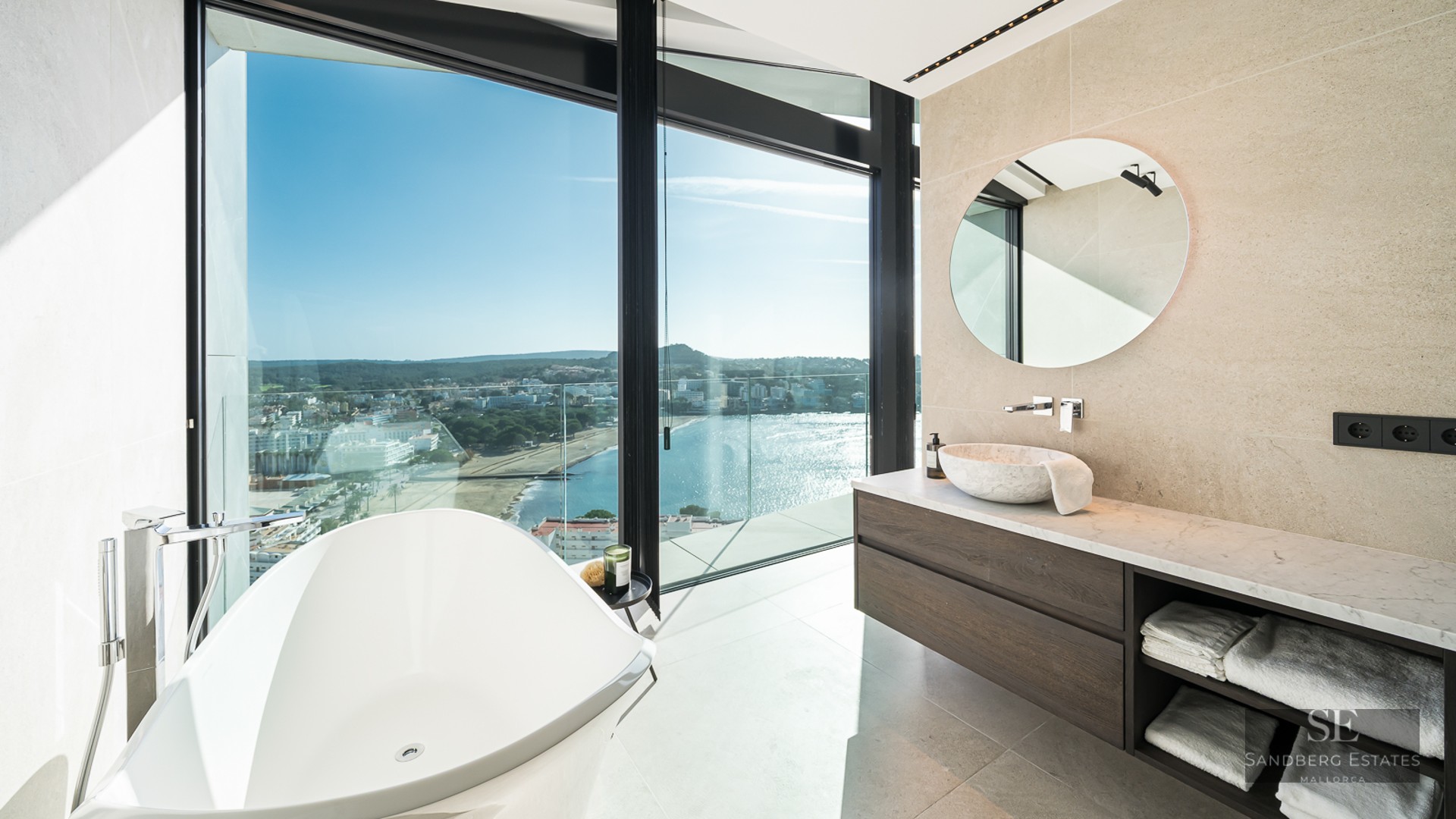 A modern bathroom featuring a white freestanding tub and large windows overlooking the ocean and coastline.