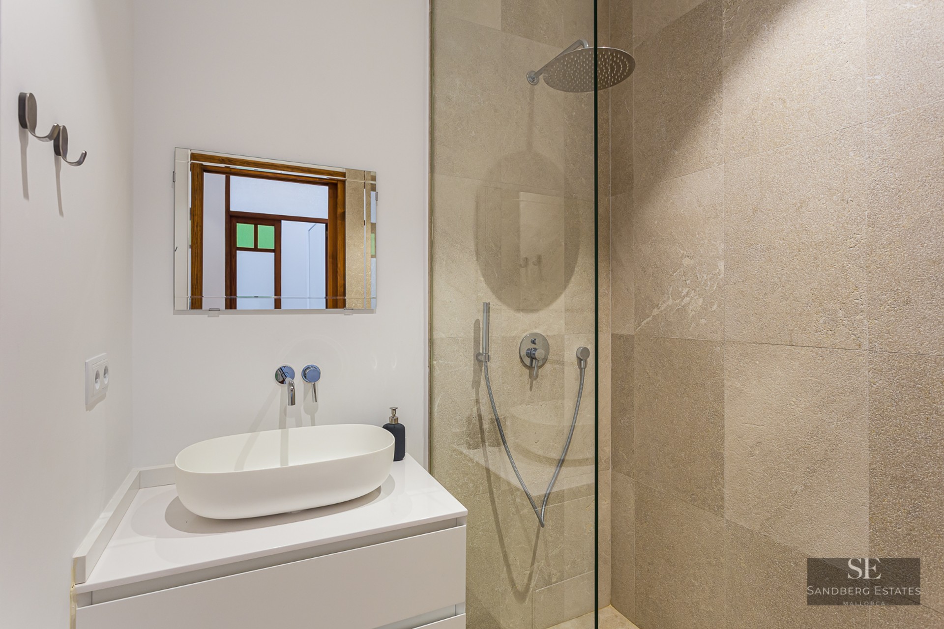 Modern bathroom featuring a white vessel sink on a white vanity and a walk-in shower with beige stone tiles.