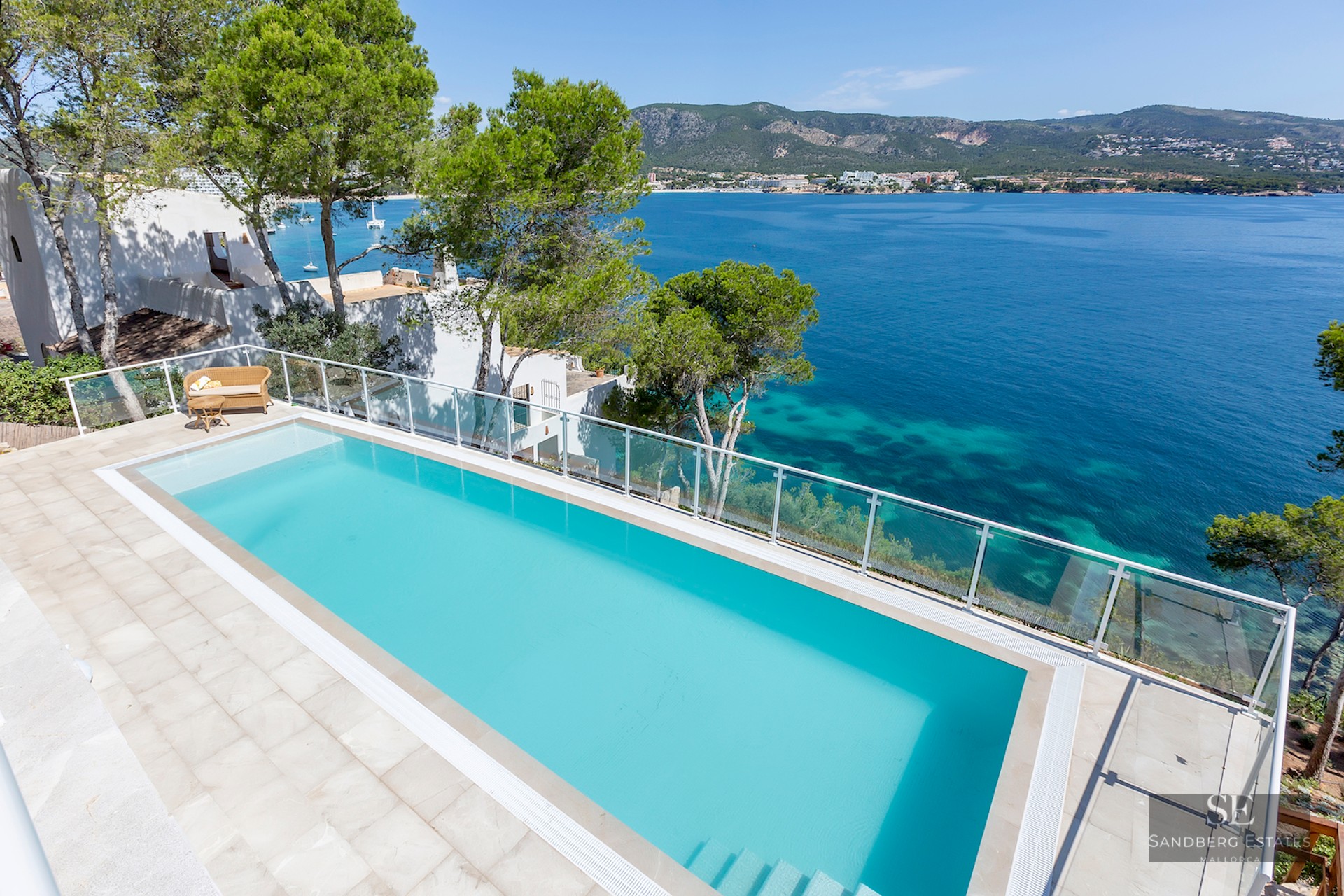An elevated view of a turquoise infinity pool overlooking the Mediterranean sea with mountains in the background.