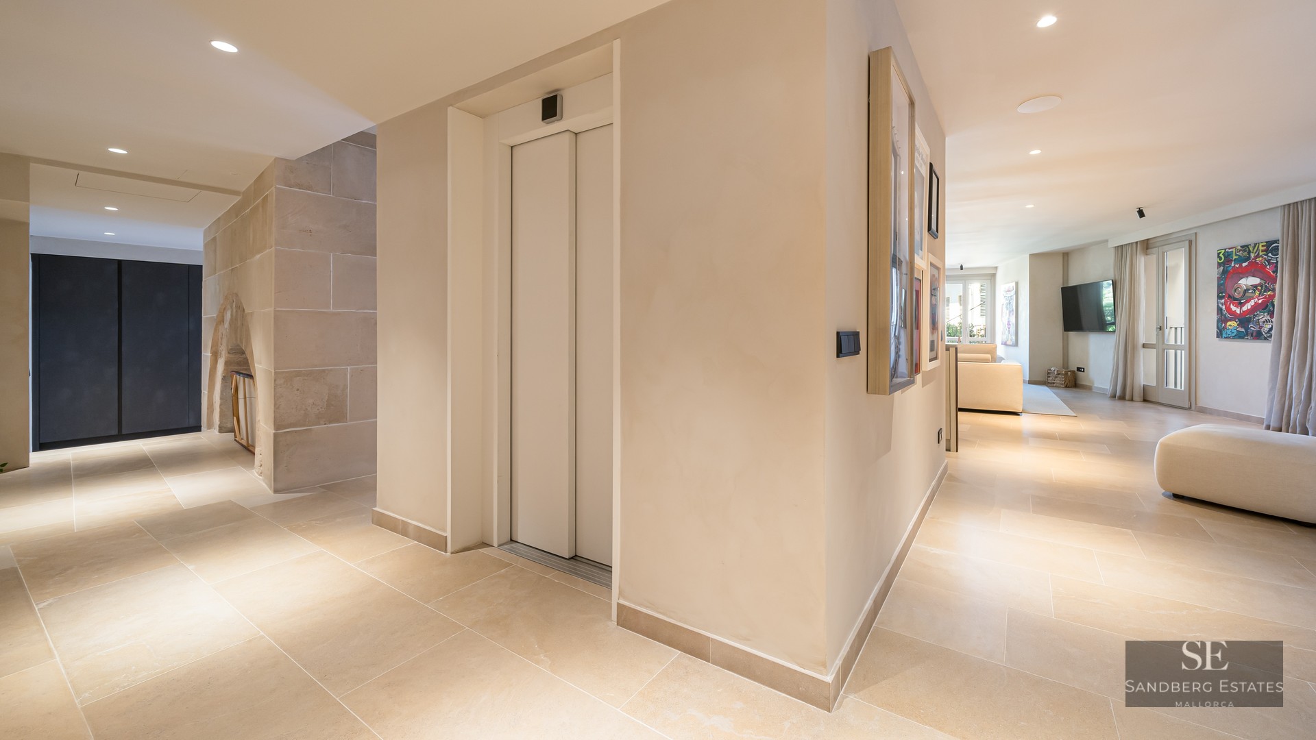 Spacious modern home entrance featuring a private elevator, beige stone floors, and a view into a bright living room.