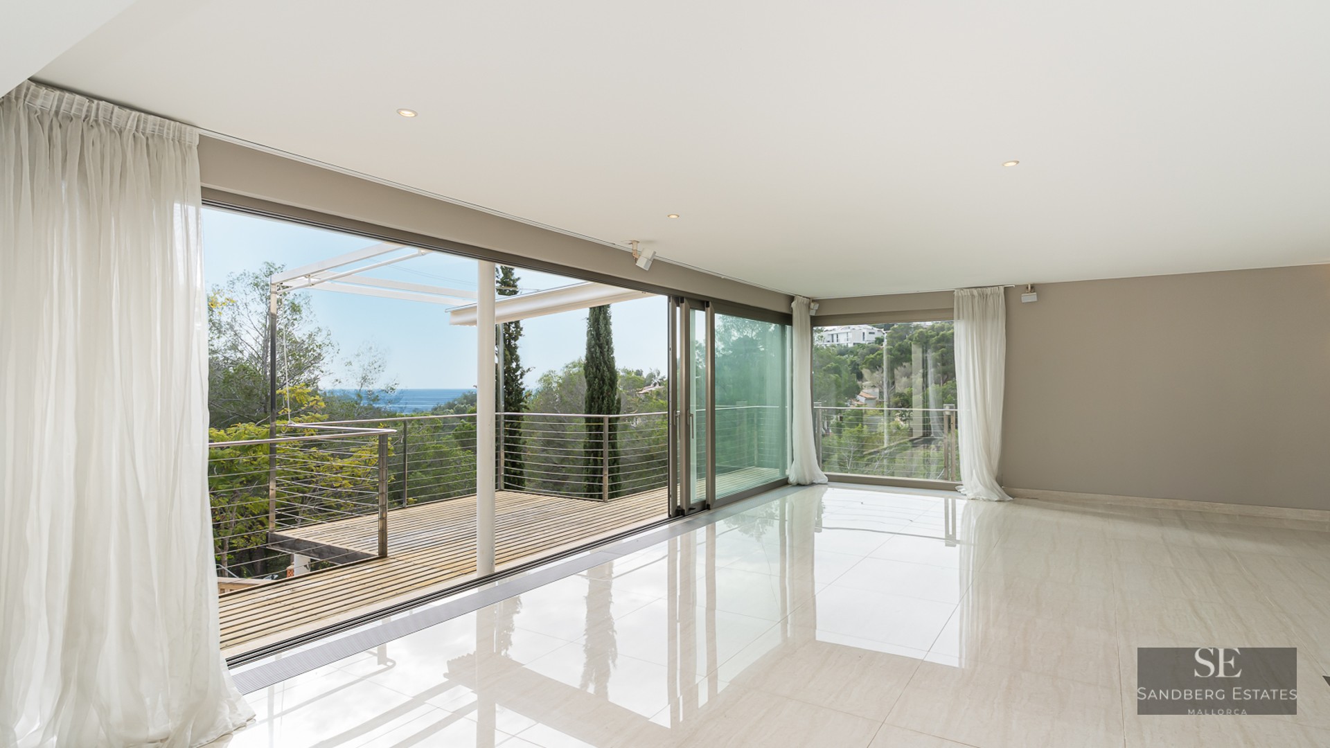 Bright, empty modern living room with polished floors and glass sliding doors opening to a terrace with sea views.