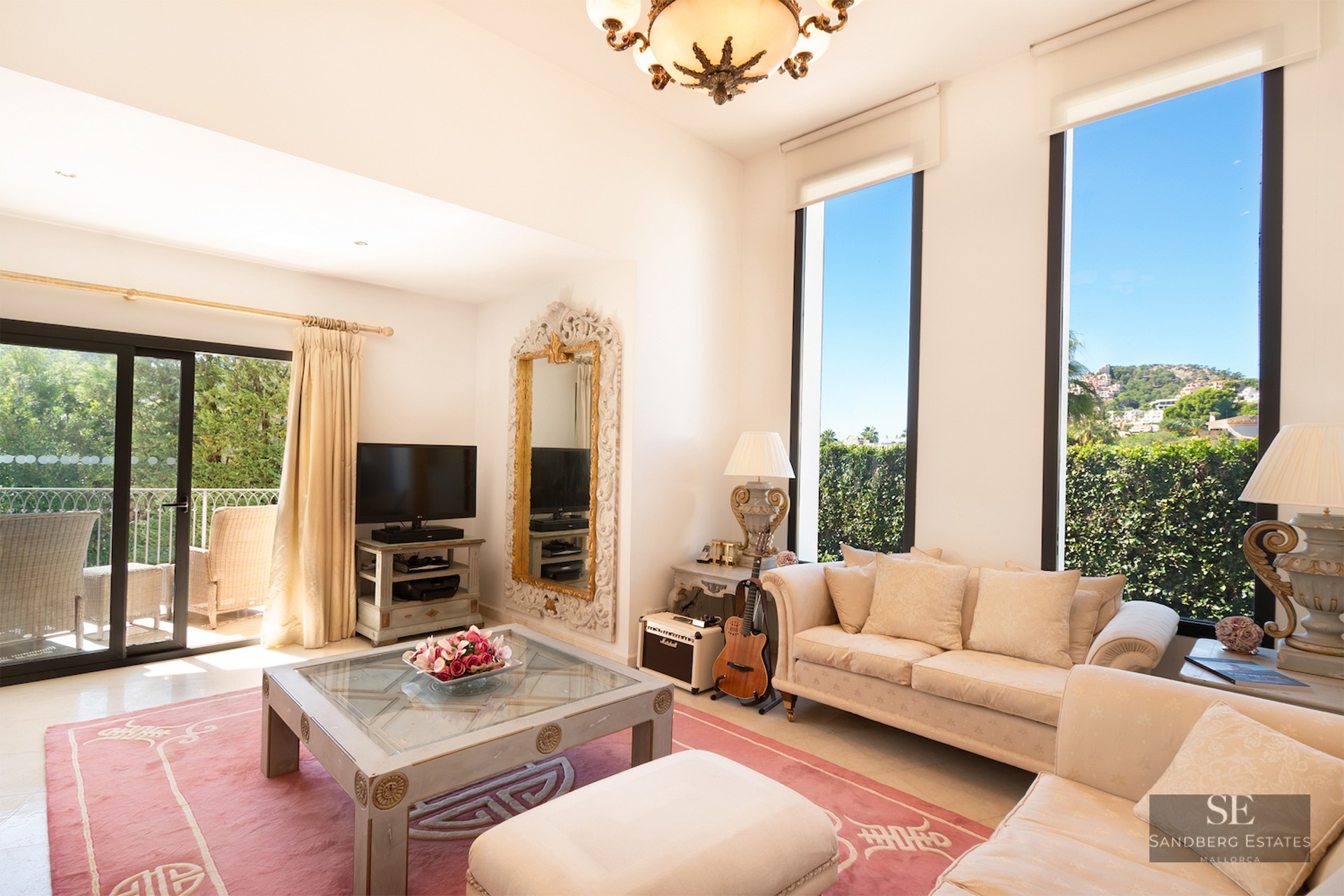 Bright living room with cream sofas, a pink rug, large vertical windows, and a sliding door leading to a balcony.