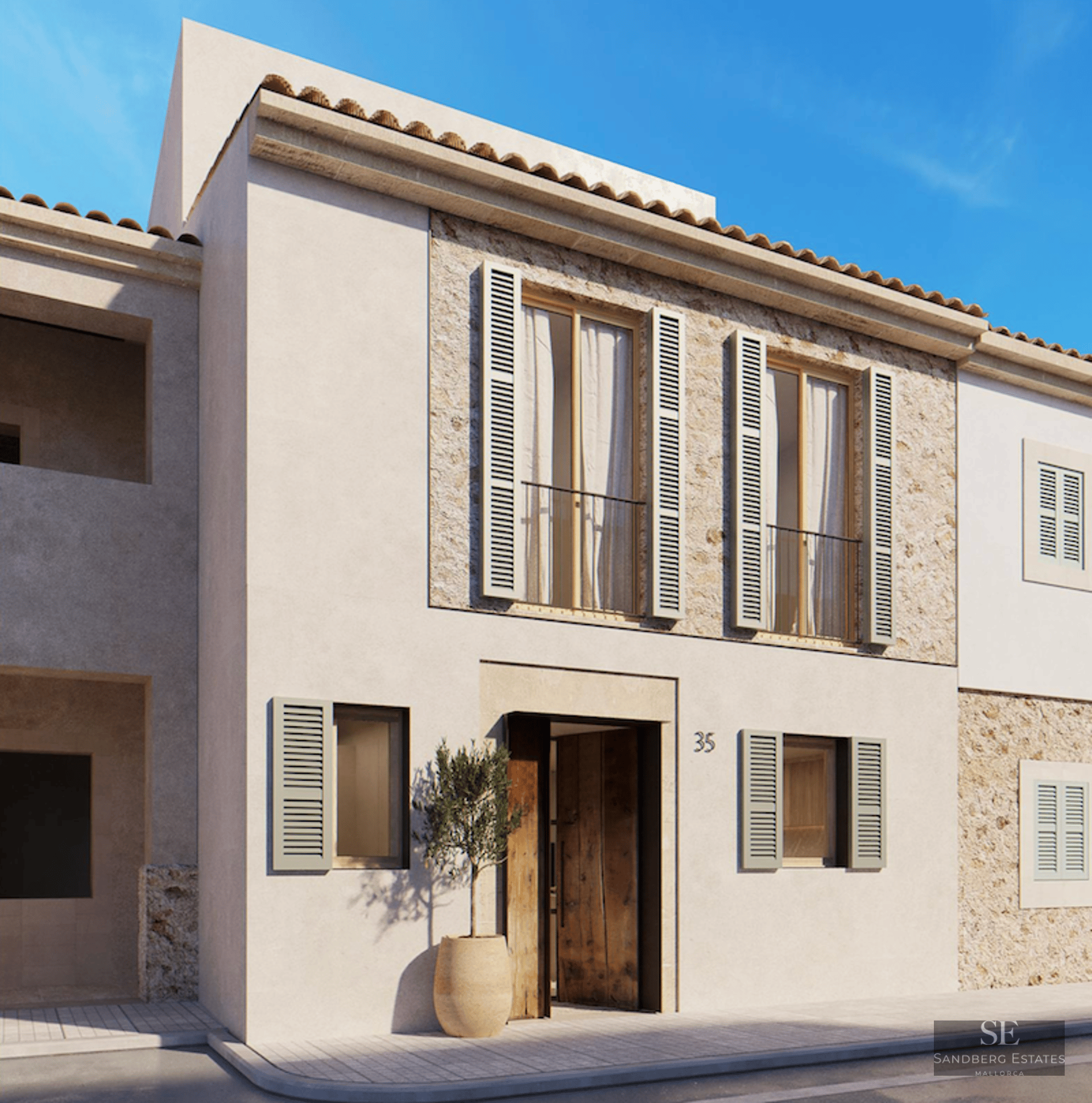 Beige stucco building with sage green shutters, natural stone accents, and a wooden door under a clear blue sky.
