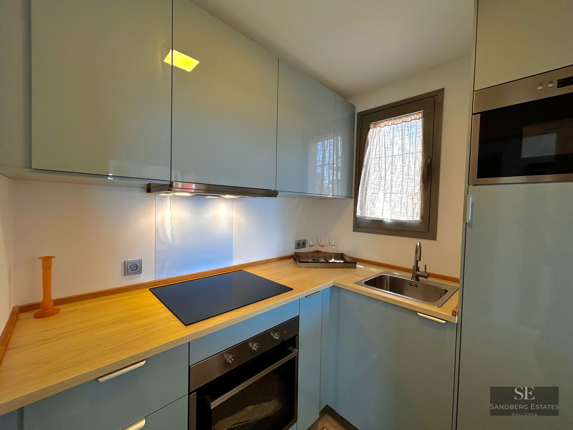 Modern kitchen featuring glossy light blue cabinets, light wood countertops, induction hob, and stainless steel sink.