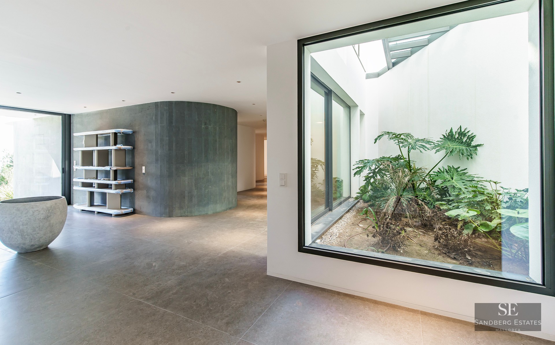 Modern hallway featuring a curved grey stone wall and a large glass window looking onto an interior garden patio.