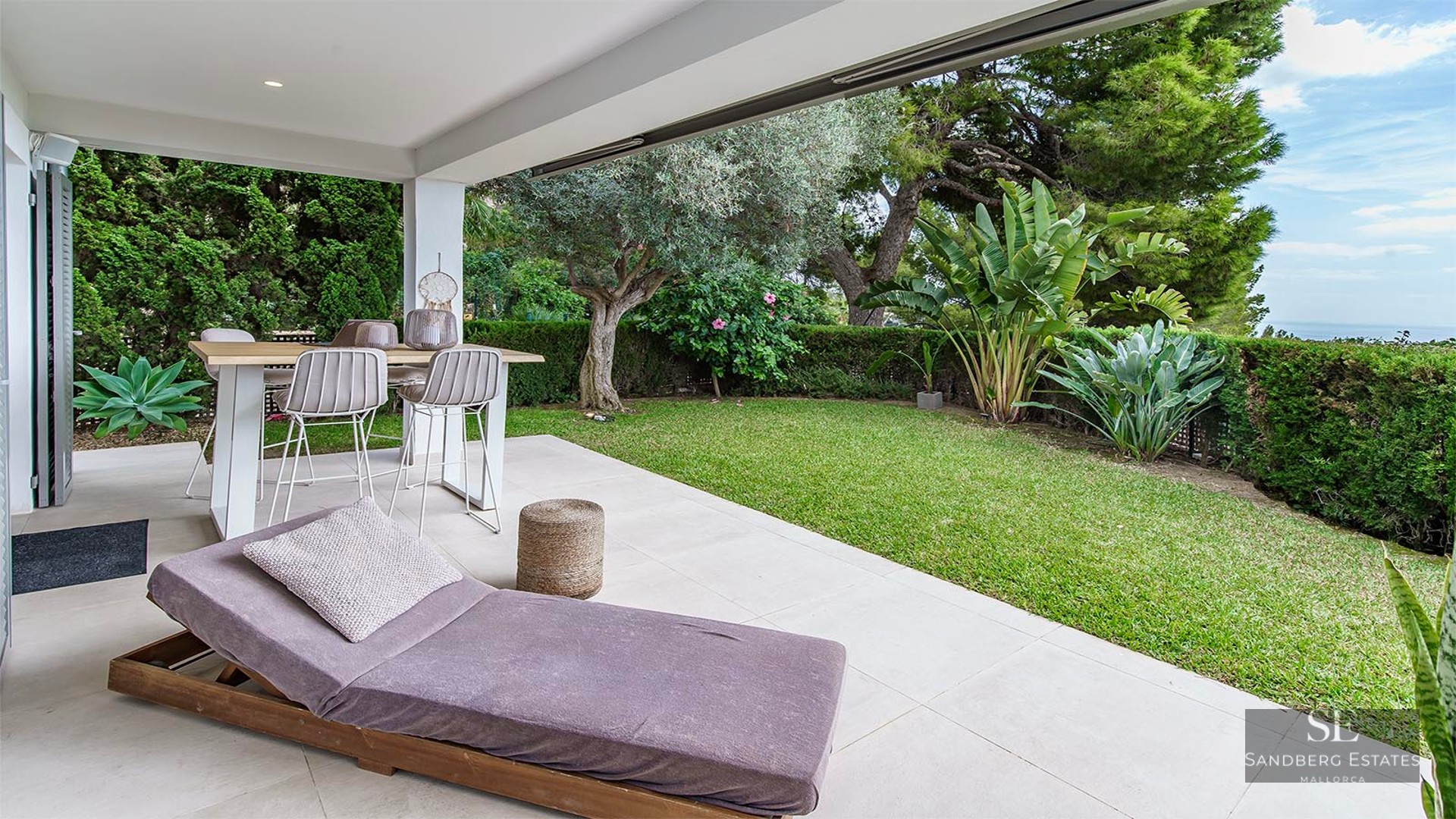 Covered terrace with dining table, sun lounger, and manicured green garden with partial sea views.