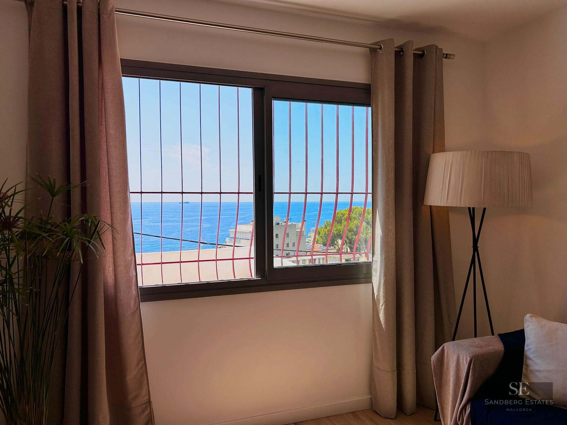 Interior view through a window with security bars looking out over the blue sea and clear sky.