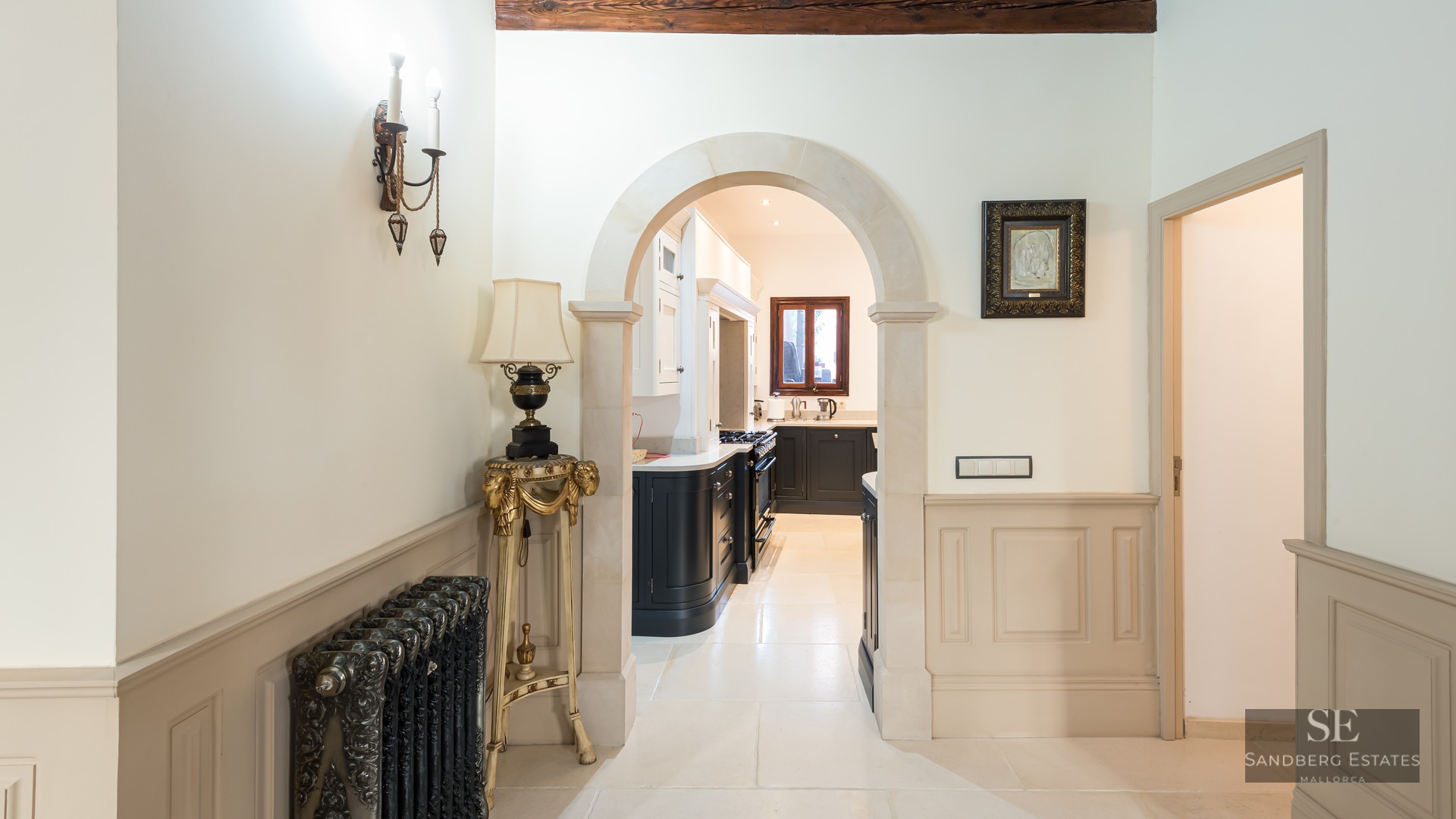 Elegant hallway with a stone archway leading to a kitchen, featuring an ornate radiator and classic wainscoting.