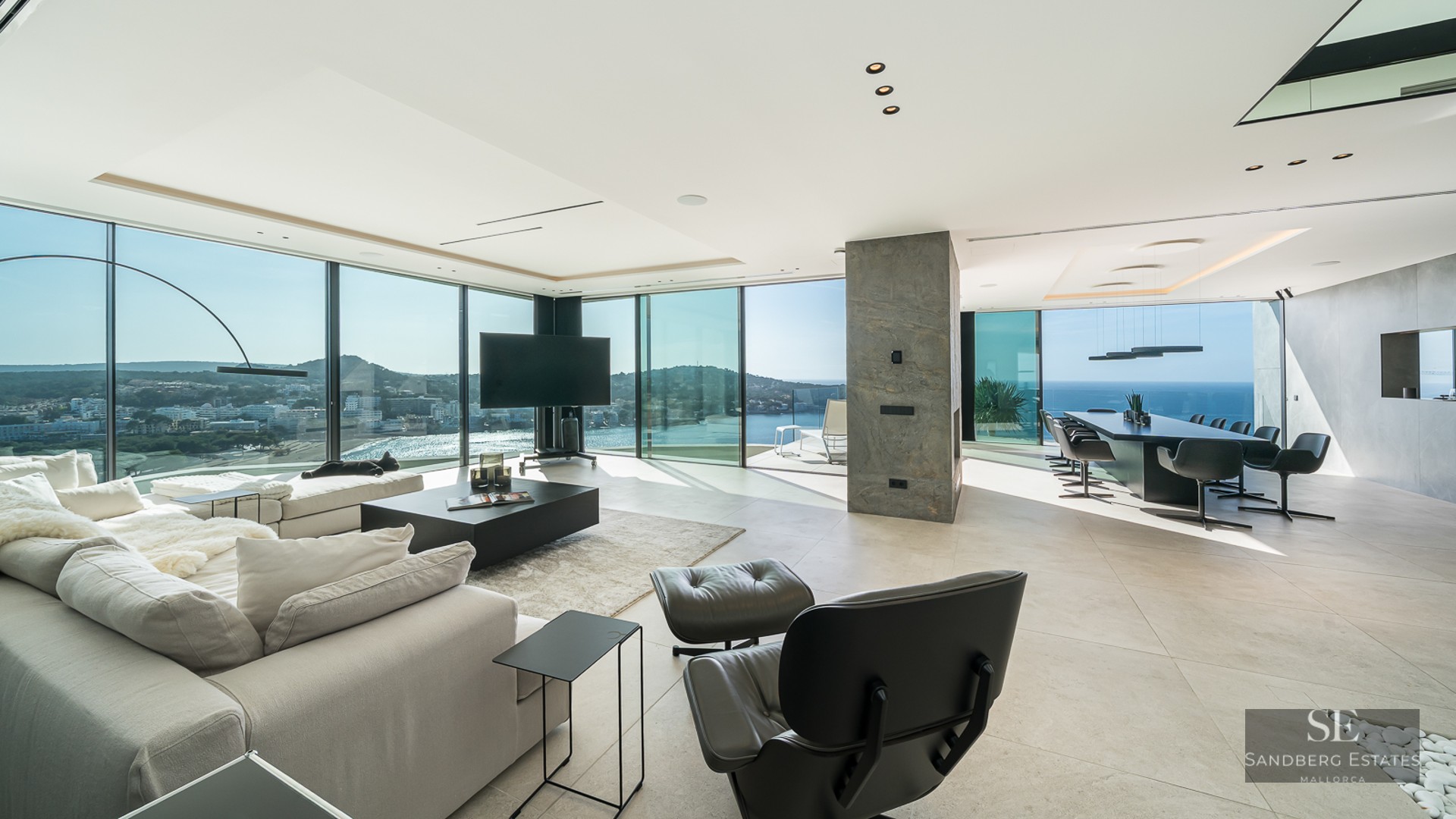 Spacious modern living room with floor-to-ceiling windows overlooking a Mediterranean bay and sea.