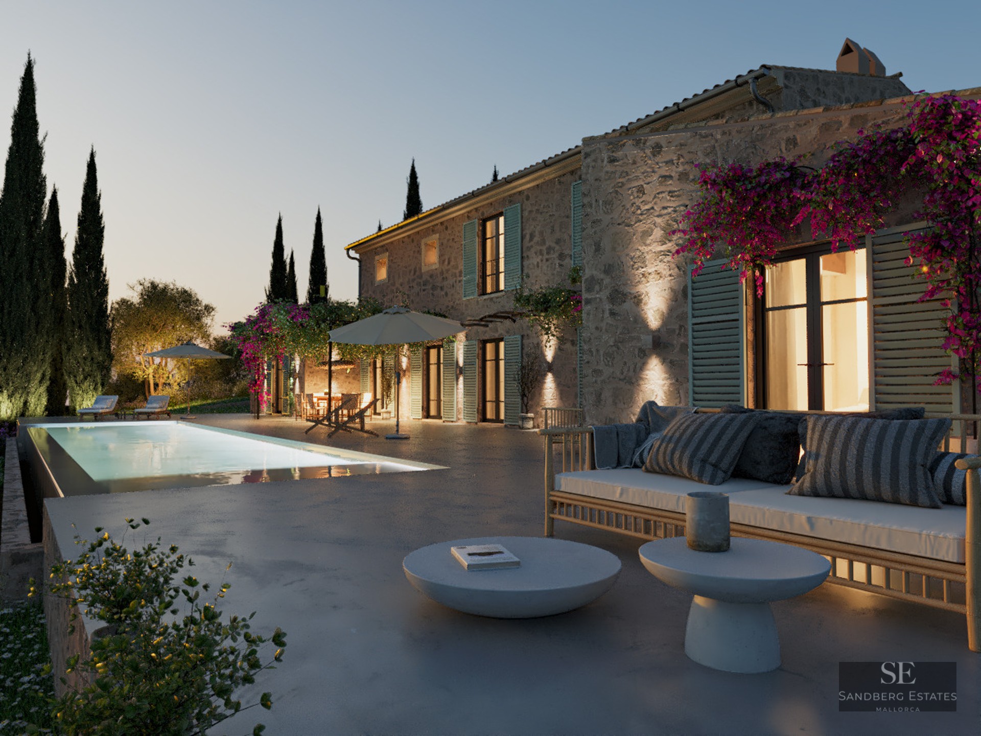 Stone villa at dusk featuring a glowing swimming pool, modern terrace furniture, and cypress trees under a twilight sky.