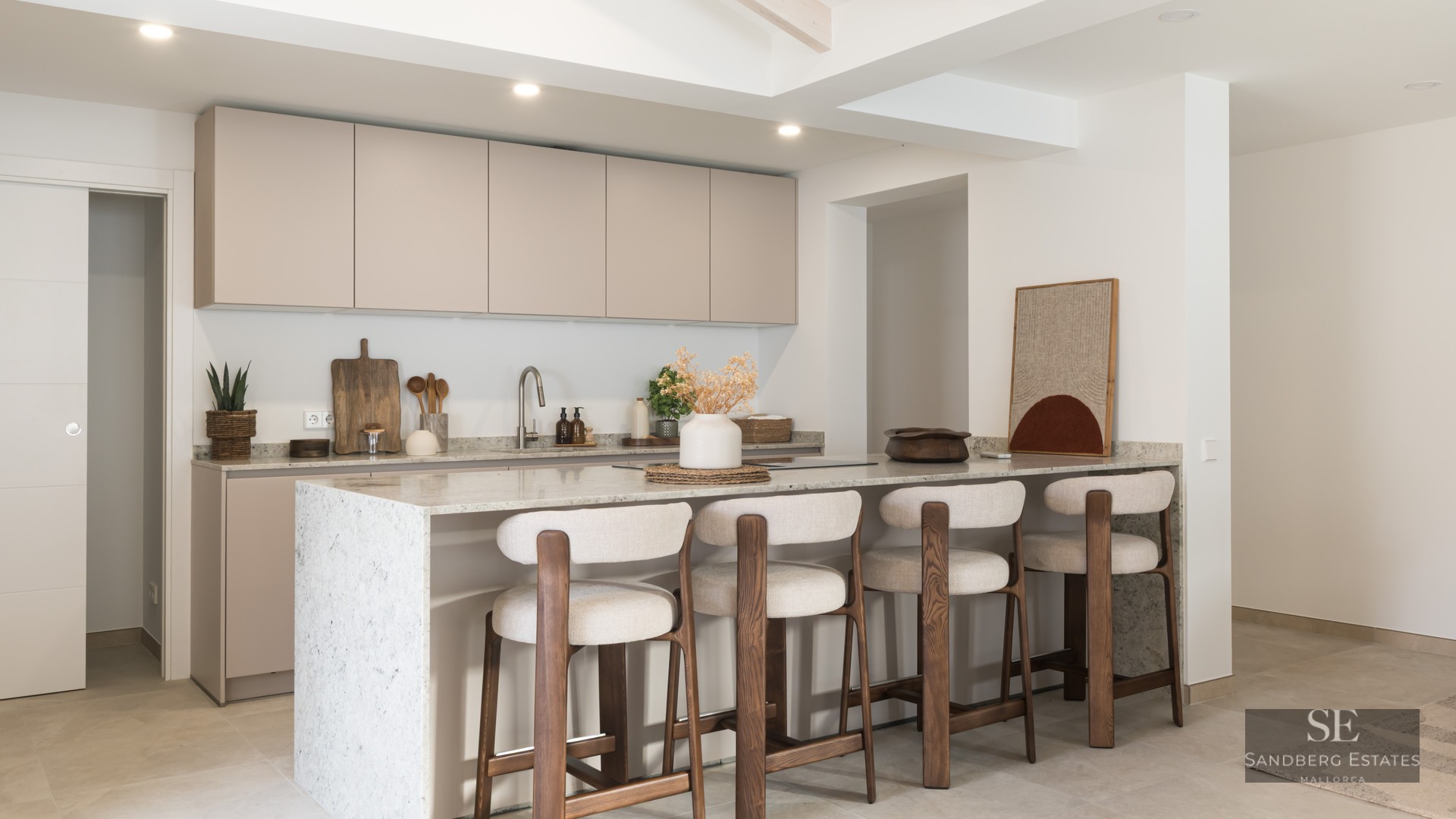 A contemporary kitchen featuring beige cabinetry, a white stone island, and four wood and fabric bar stools.