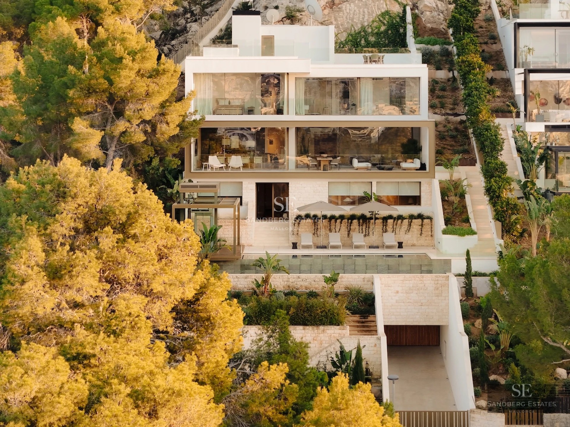 View of a modern villa featuring an infinity pool, manicured gardens, and minimalist architecture. Warm lighting and elegant outdoor furniture.