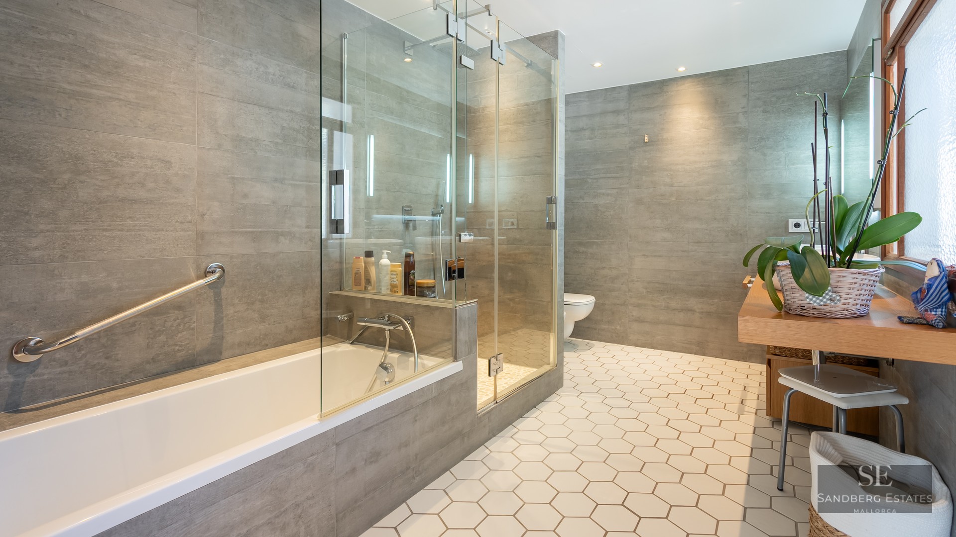 Modern bathroom with white hexagonal floor tiles, a glass-enclosed shower, a bathtub, and grey wall tiles.