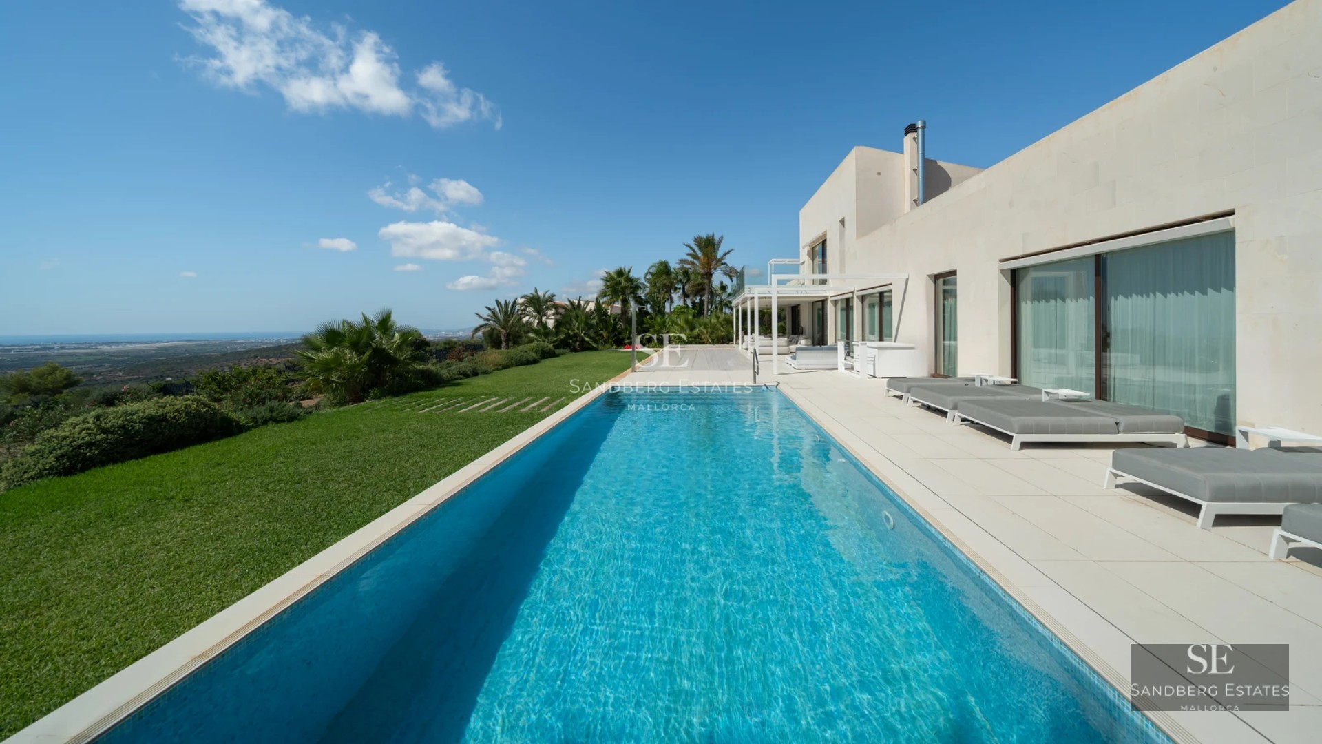 Pool view featuring sun loungers, palm trees, and a modern design house with large windows. Luxurious and minimalist exterior.