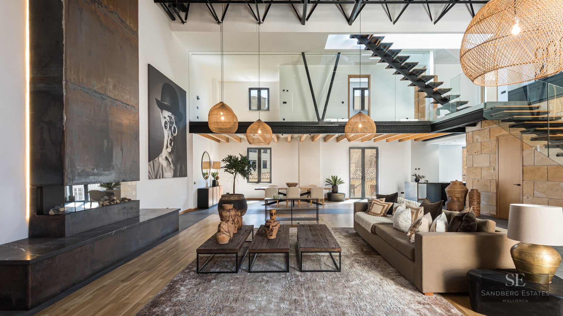 Spacious modern living room with a steel fireplace, high ceilings, floating staircase, and designer decor.