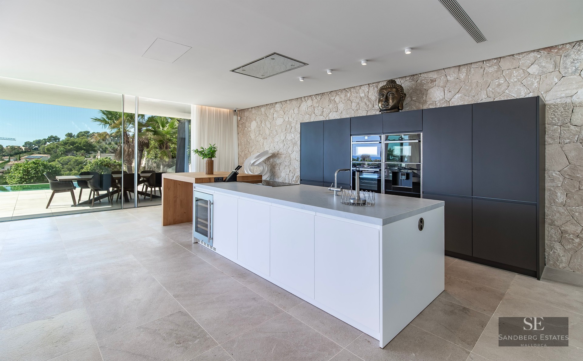 Luxury kitchen featuring a white island, integrated appliances, a rustic stone wall, and glass doors to a terrace.